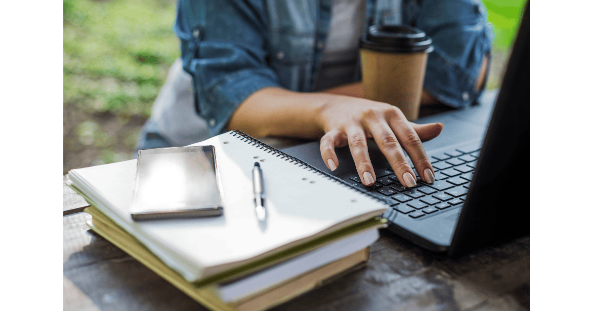 Woman typing About page on computer with coffee and notebook