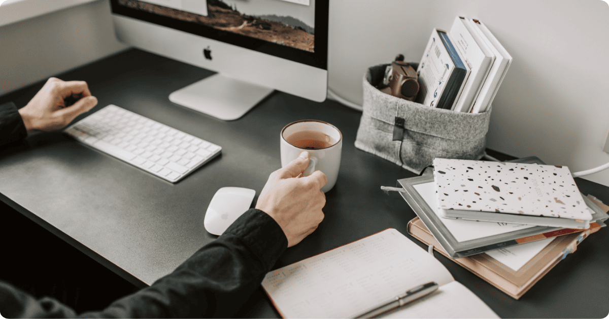person with tea at desk with notebooks and planners