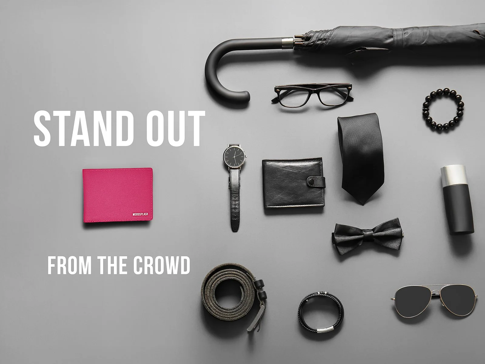 Minimal black accessories layout with a bright pink wallet and “Stand Out From the Crowd” message.