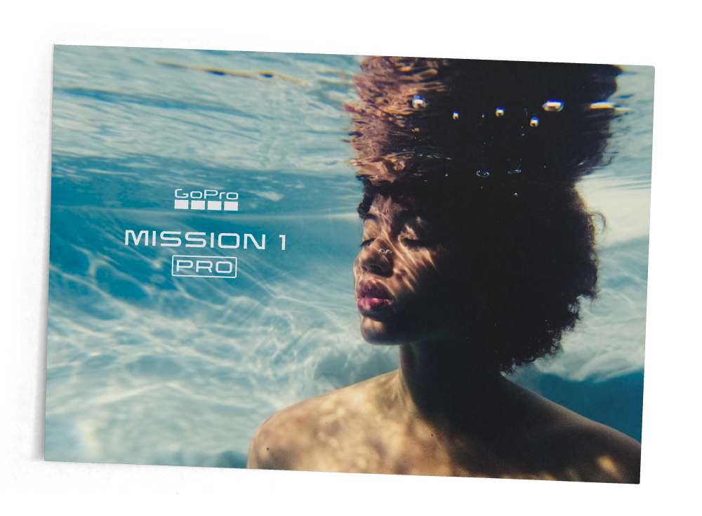 Young woman with curly hair submerged underwater with text overlay of GoPro Mission 1 Pro.