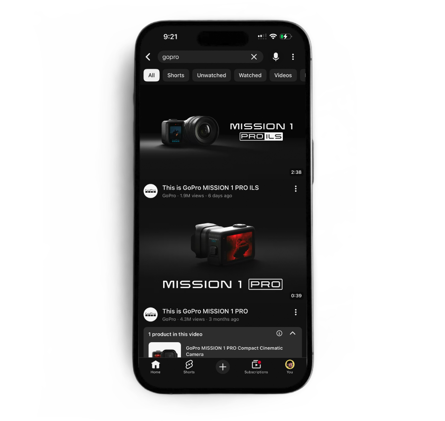 A smartphone screen displays a YouTube search results page for 'GoPro,' showing videos about the GoPro MISSION 1 PRO camera, with a black background and white splatters around the phone.