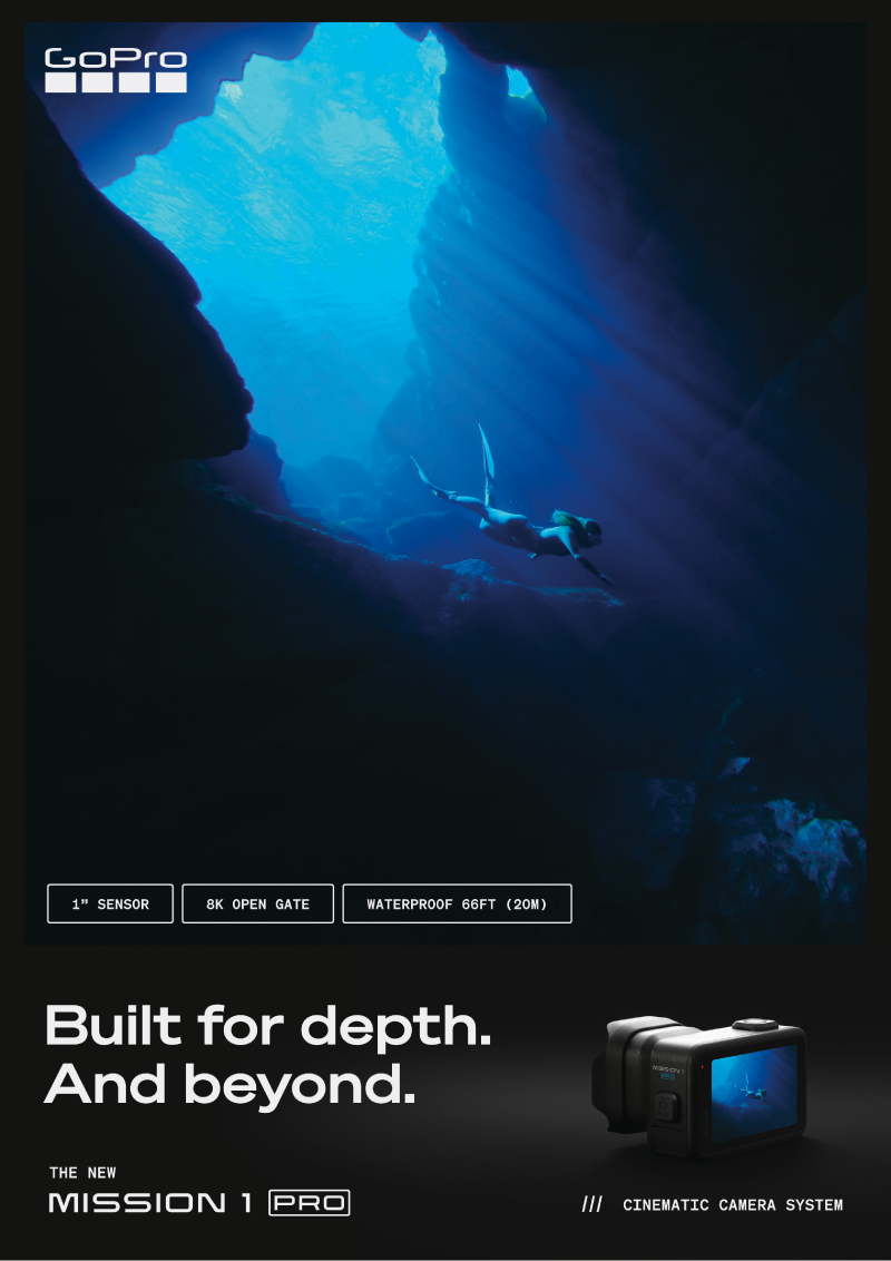An underwater scene with a diver swimming through a deep, rocky cave, illuminated by sunlight filtering down from above.
