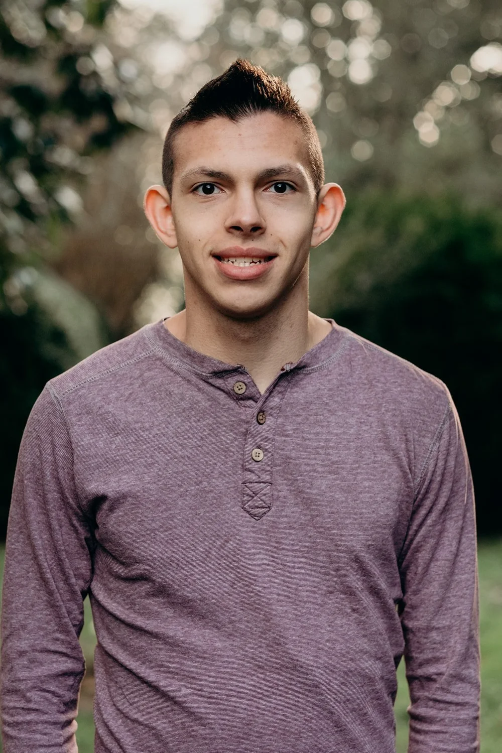 Nate, smiling, in a purple henley shirt outdoors