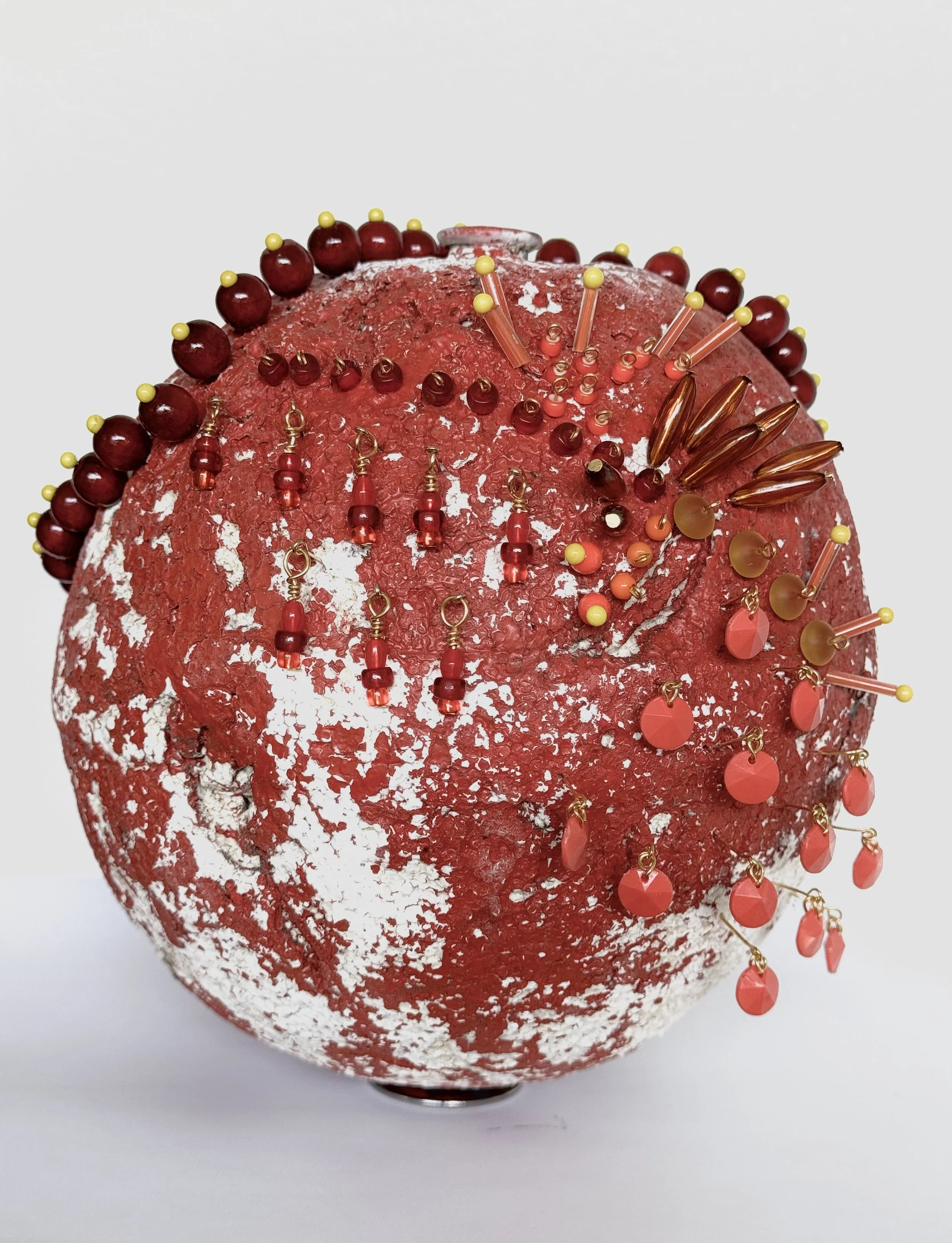 Decorative red and white spherical object resembling a vintage globe decorated with various small, colorful beads and pins around the surface.