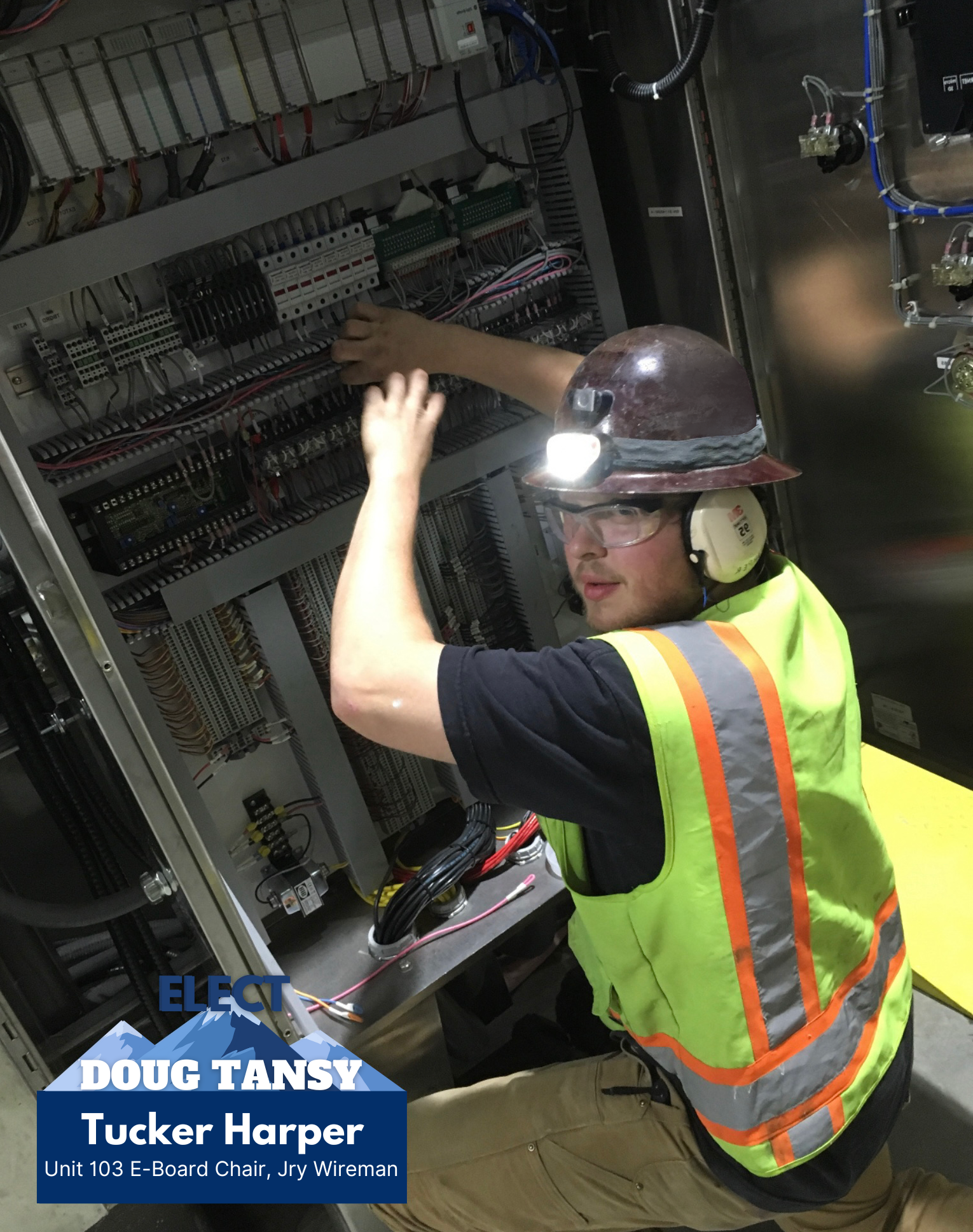 A technician wearing a hard hat, safety glasses, and a high-visibility vest working on electrical panels with numerous wires and components inside an industrial setting.