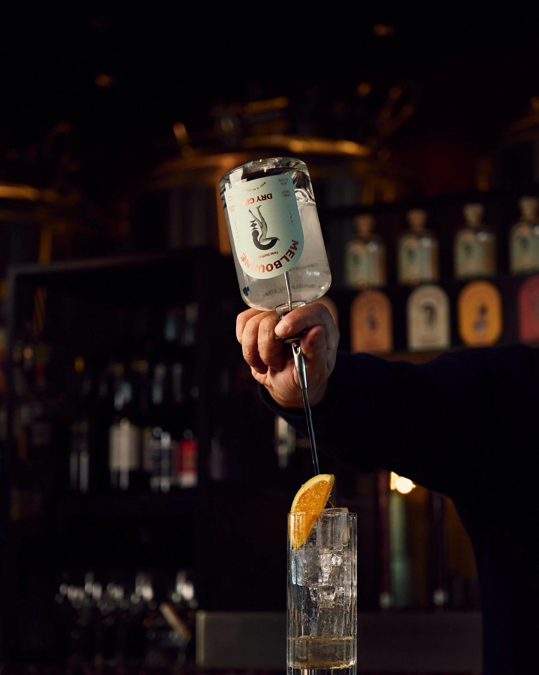 Bartender pouring gin into a cocktail with ice and orange slice