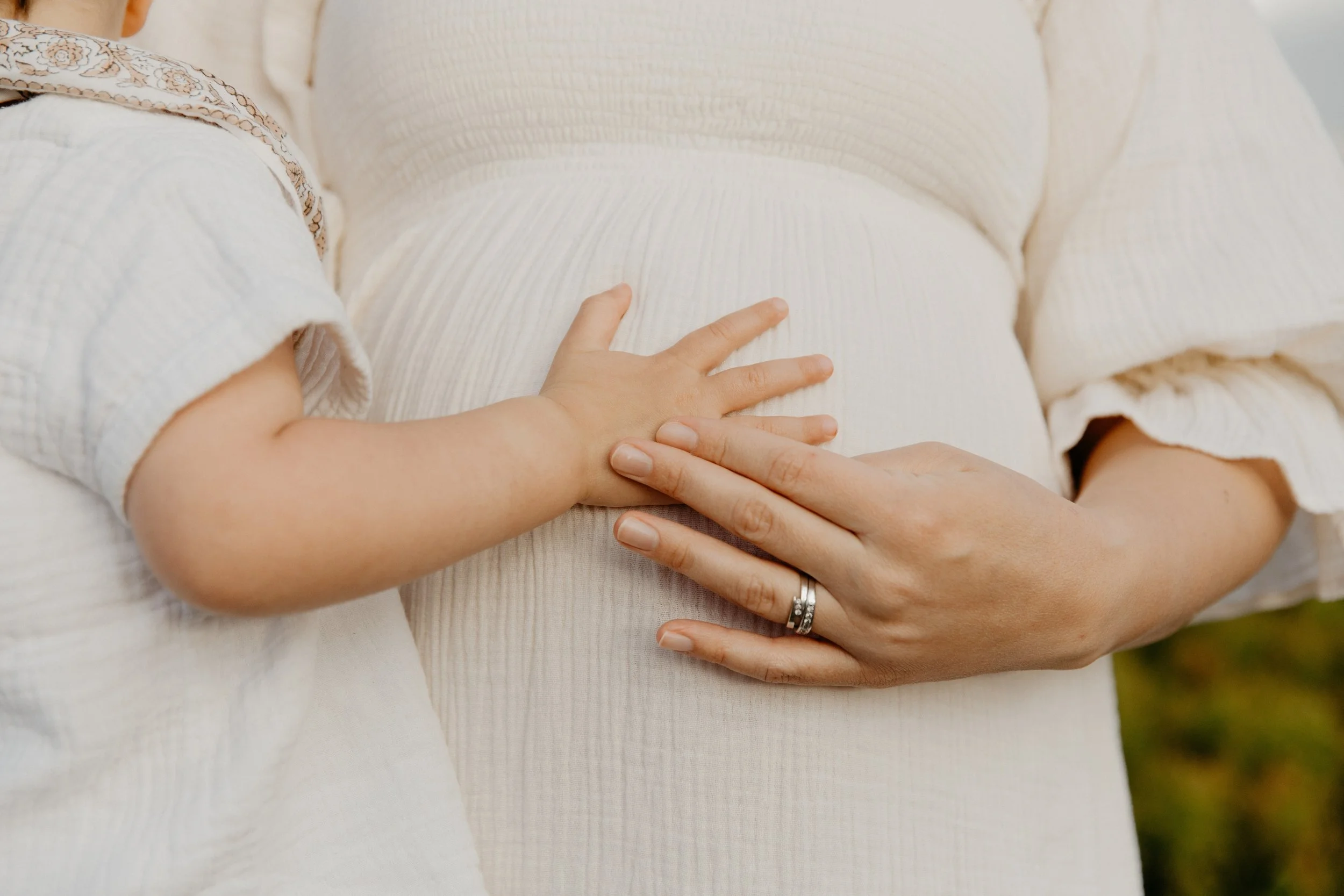 A pregnant woman placing her younger daughters hand on her stomach