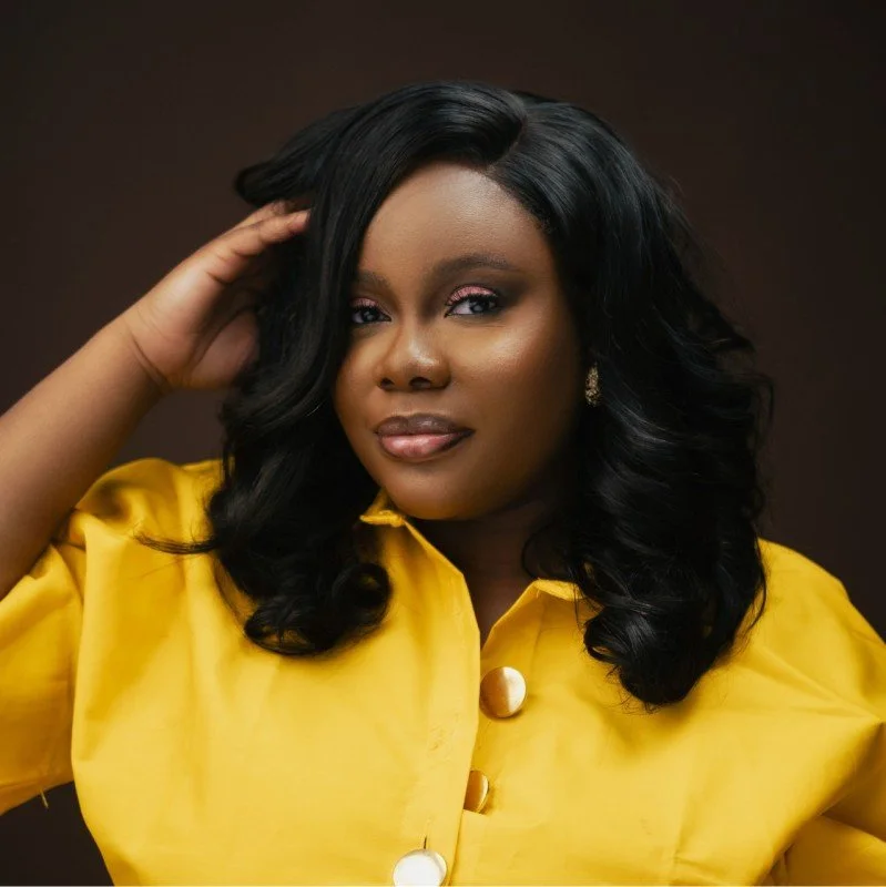 A black woman wearing a yellow blouse with her hand in her hair