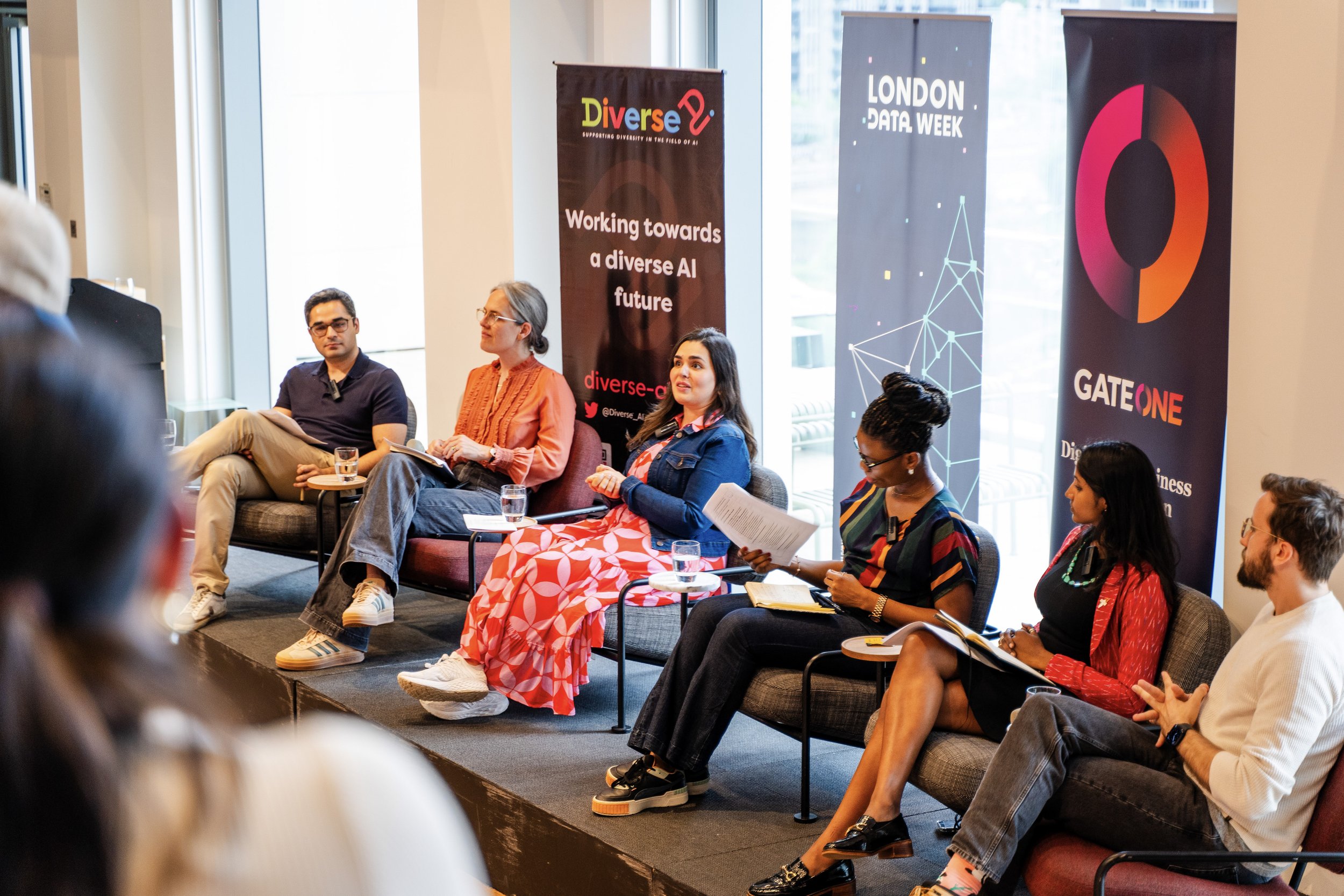 An image of 5 people sitting down facing a crowd