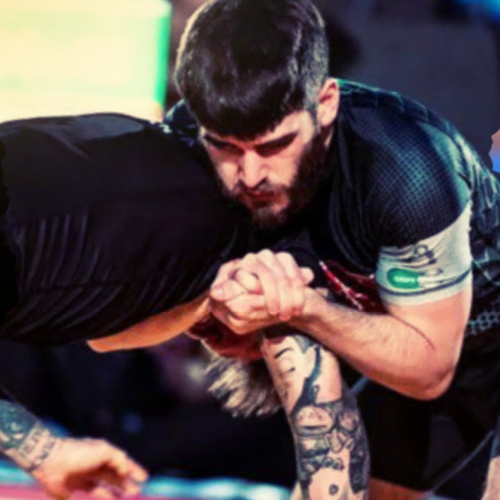 Two men competing in arm wrestling, with one man gripping and pressing the other's arm on a wooden table.