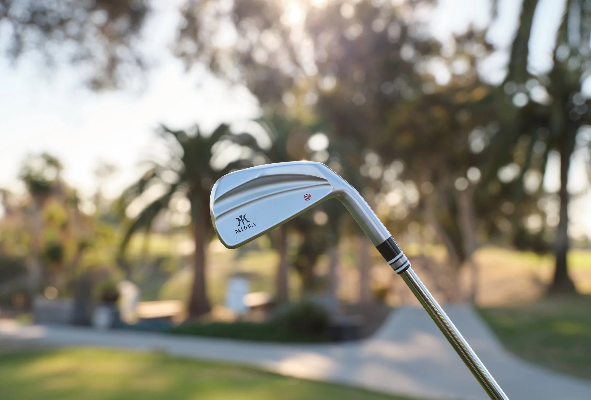 Ein Golf-Schläger auf einem Golfplatz mit Bäumen im Hintergrund und Sonnenlicht.