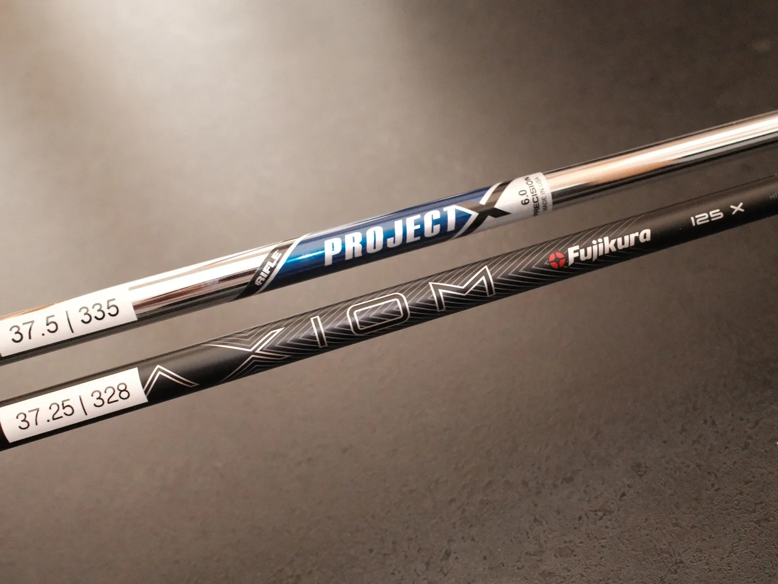 Project X und Fujikura Axiom Golfschäfte liegen nebeneinander auf einer dunklen Oberfläche.
