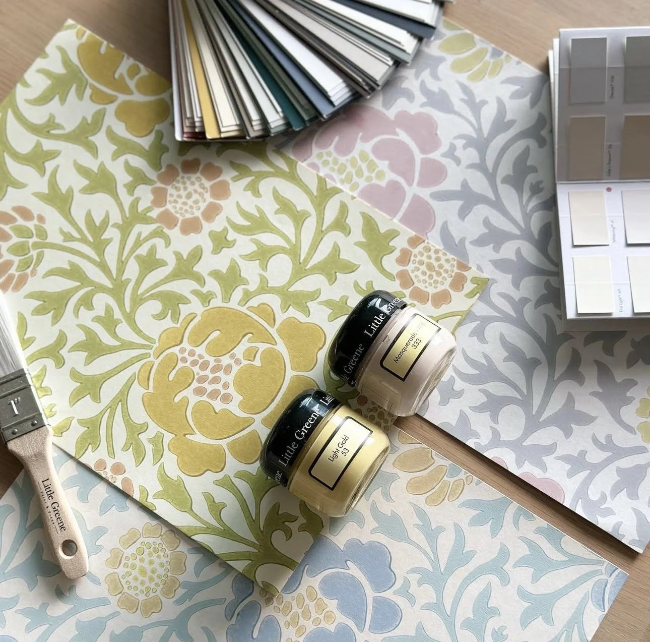 Color sample papers with floral patterns, paint jars labeled 'Light Gold' and 'Moss Green,' paintbrush labeled 'Little Greene,' and a paint color palette sample card.