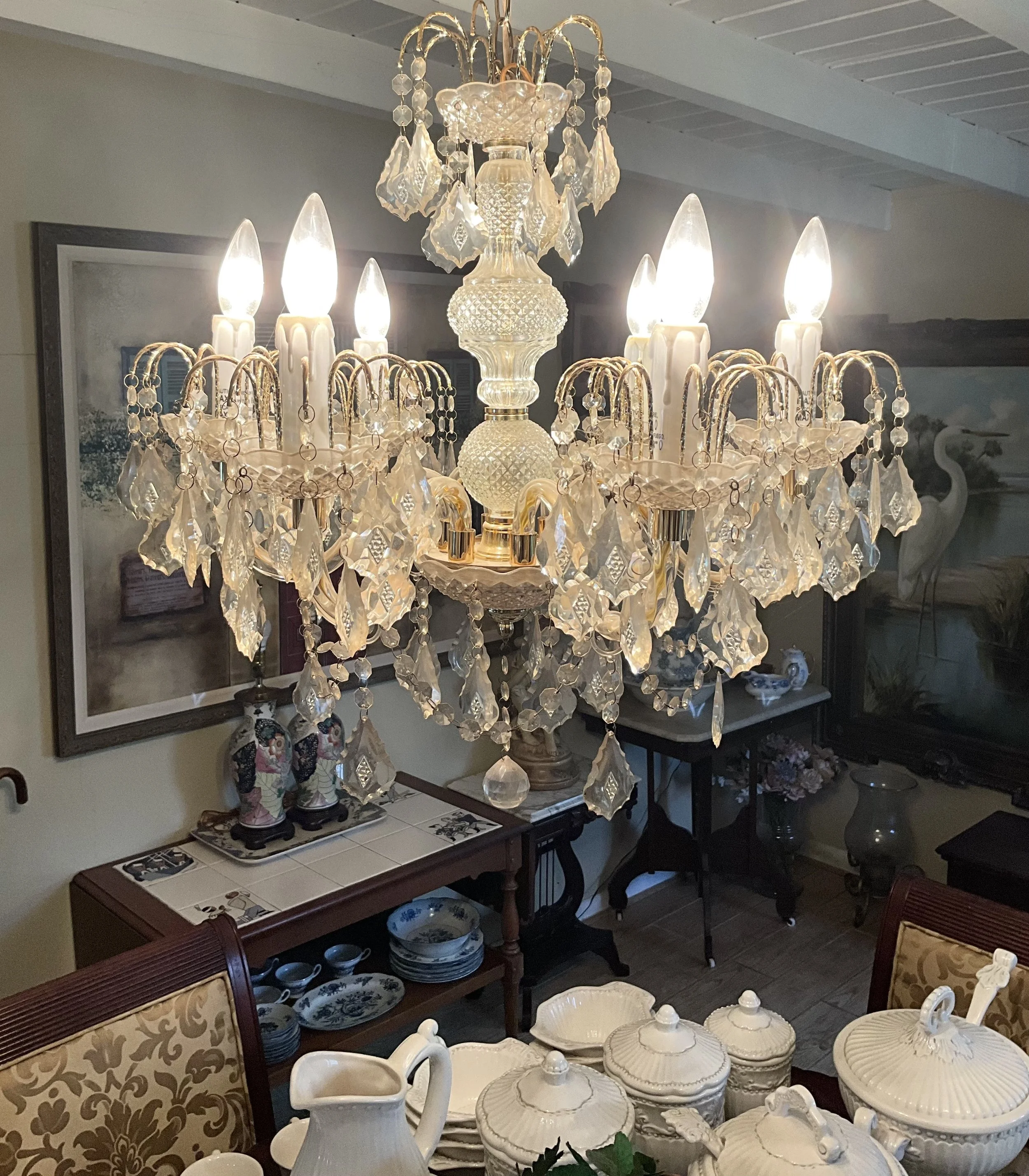 Elegant chandelier with crystal adornments hanging over a dining area with china and decorative items.