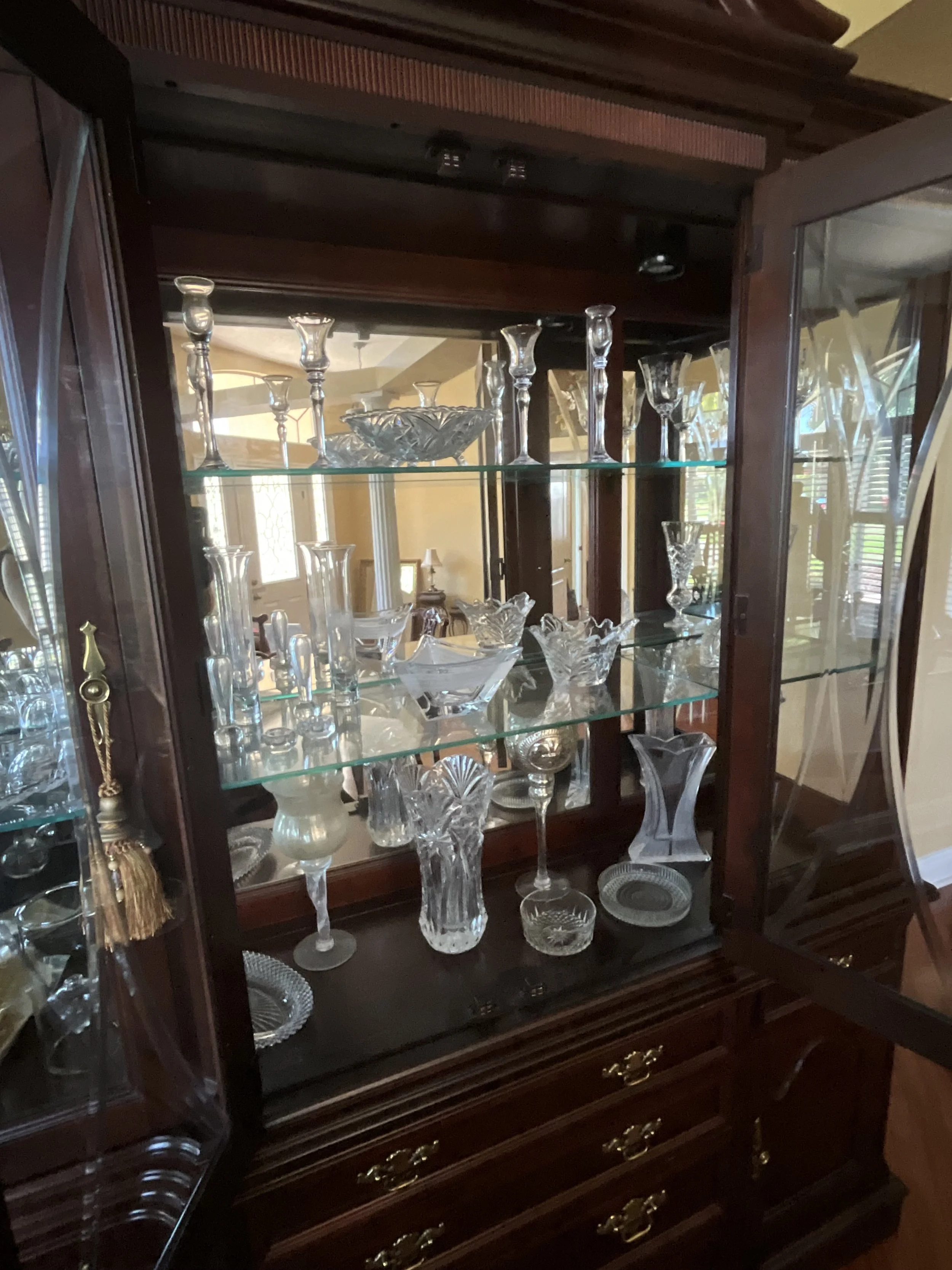 Display cabinet filled with various glassware including goblets, vases, and bowls, made of clear cut glass, inside a wooden china cabinet with glass doors and brass handles.