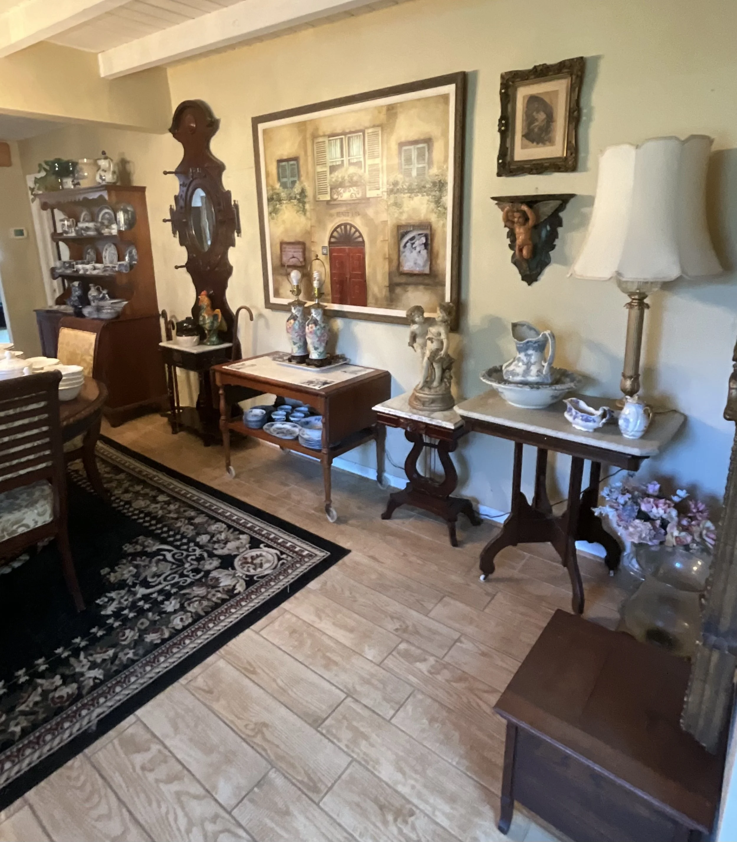 A living room corner with antique furniture, decorative porcelain vases, sculptures, paintings, a wooden clock, and a patterned area rug.