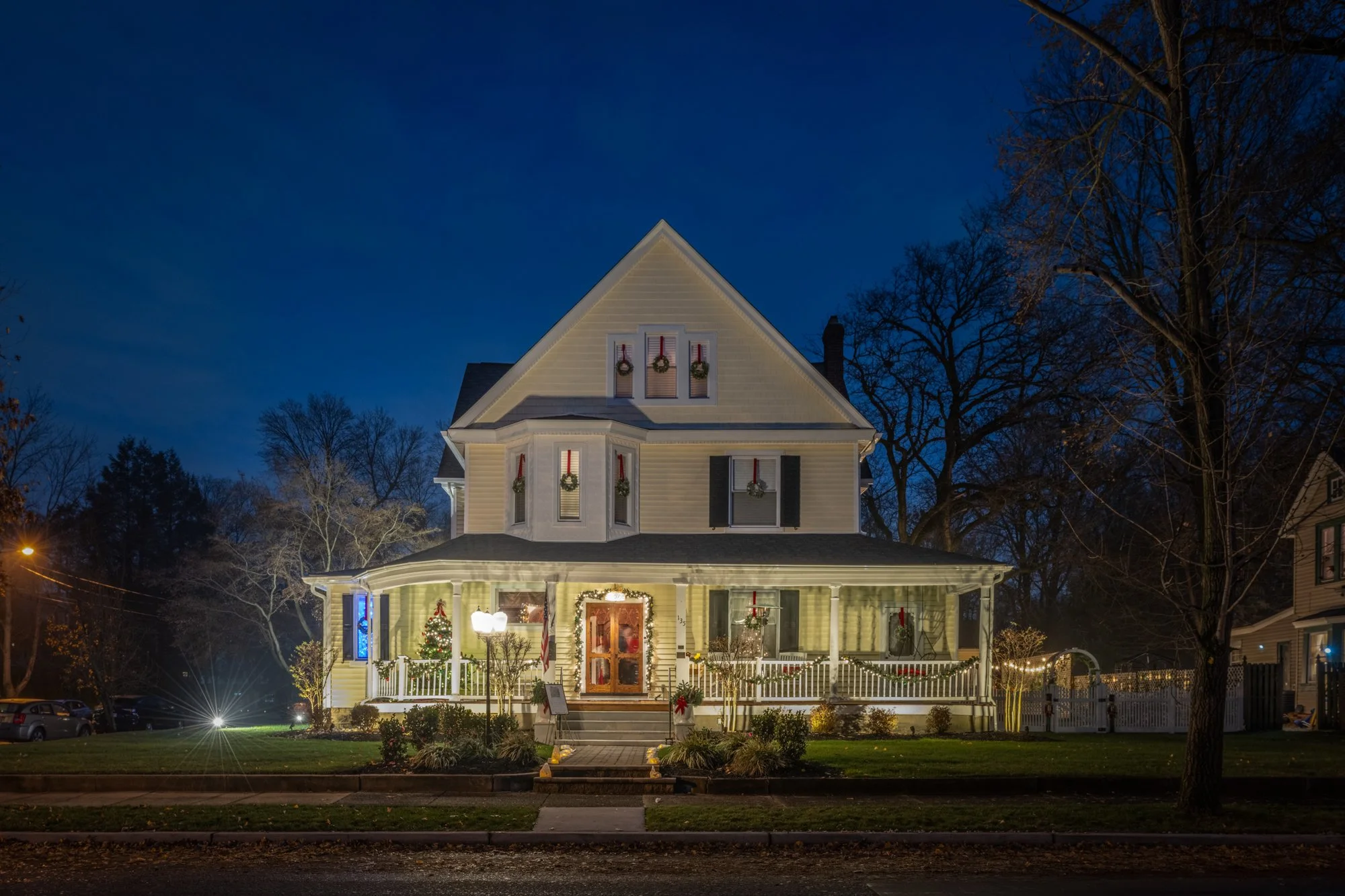 A decorated house at night with Christmas lights and wreaths, featuring a Christmas tree and illuminated porch.