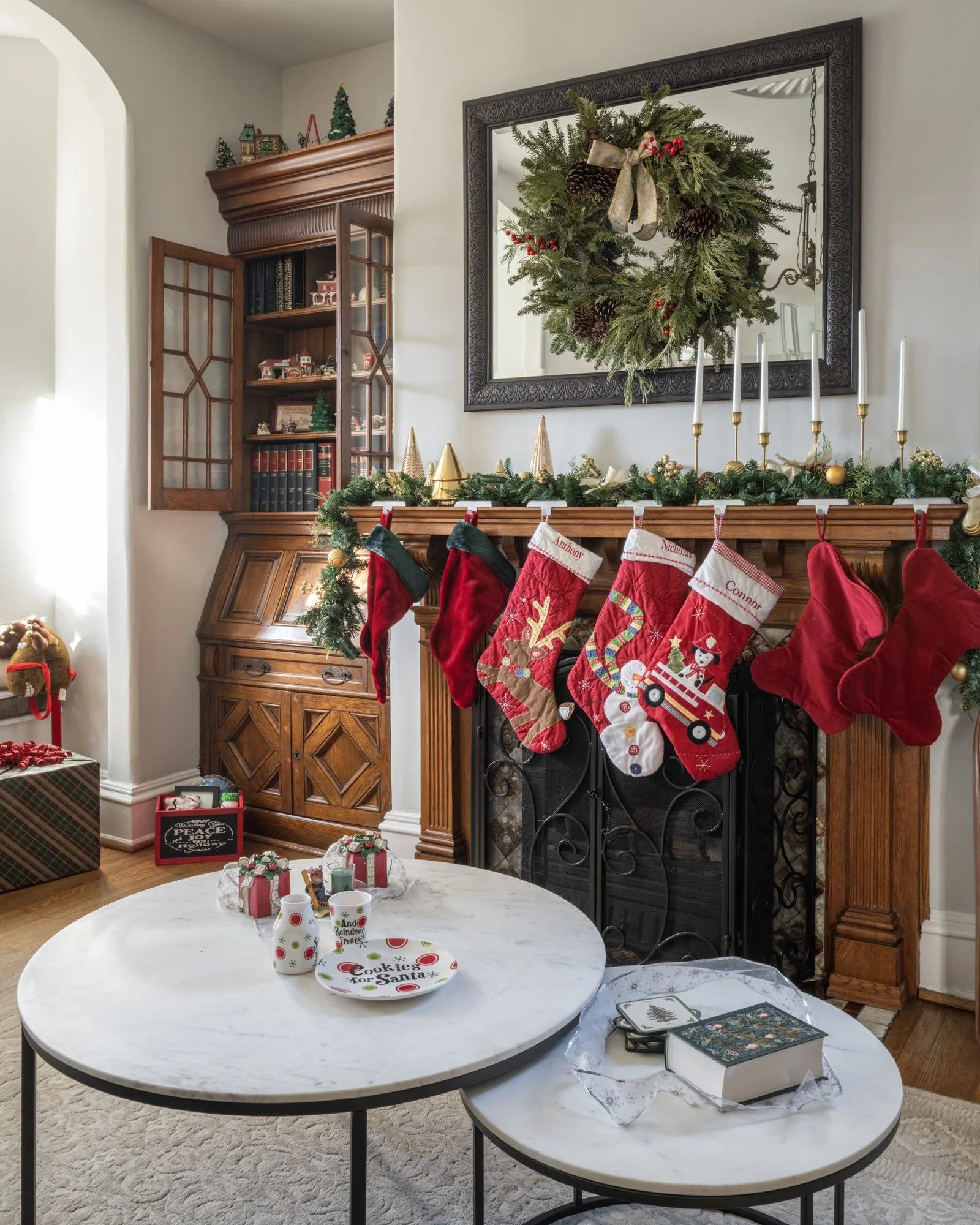 Living room fireplace decorated for Christmas with stockings hanging, a wreath, and holiday ornaments on the mantle. Christmas presents are on a table nearby.