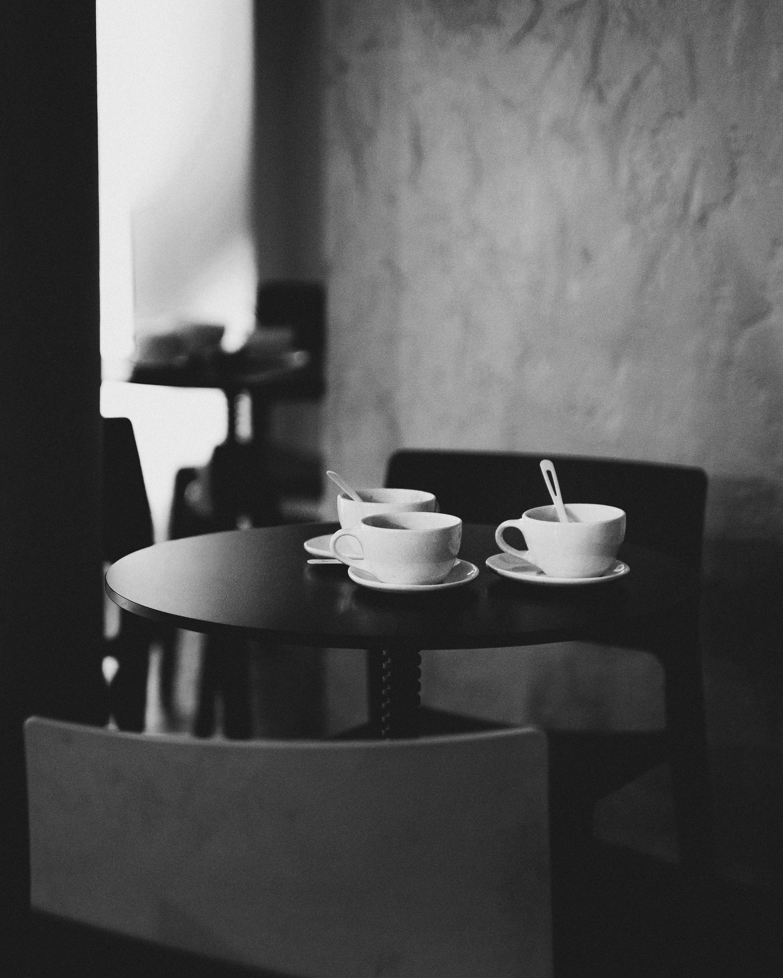Three white coffee cups with small spoons on saucers on a dark round table in a dimly lit room