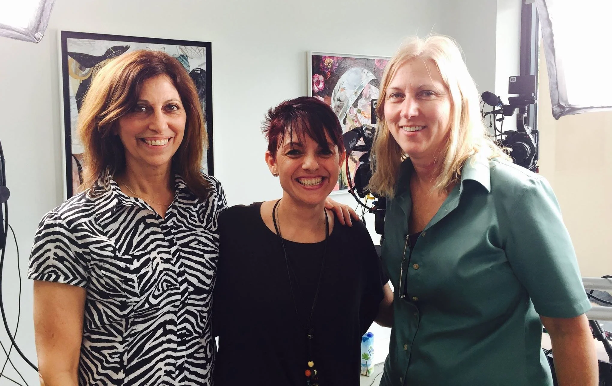 Three women smiling in a room with cameras and art in the background