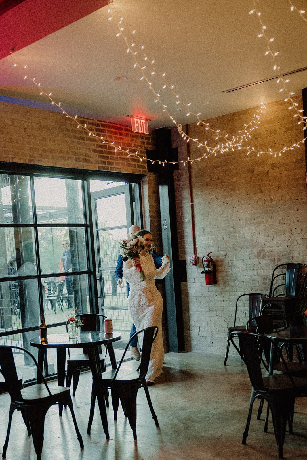 A bride entering the brick-walled event space beneath string lights at Duetts.