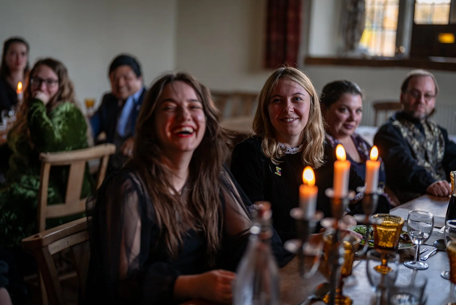 People sitting at a dining table with candles, smiling and enjoying a gathering indoors.