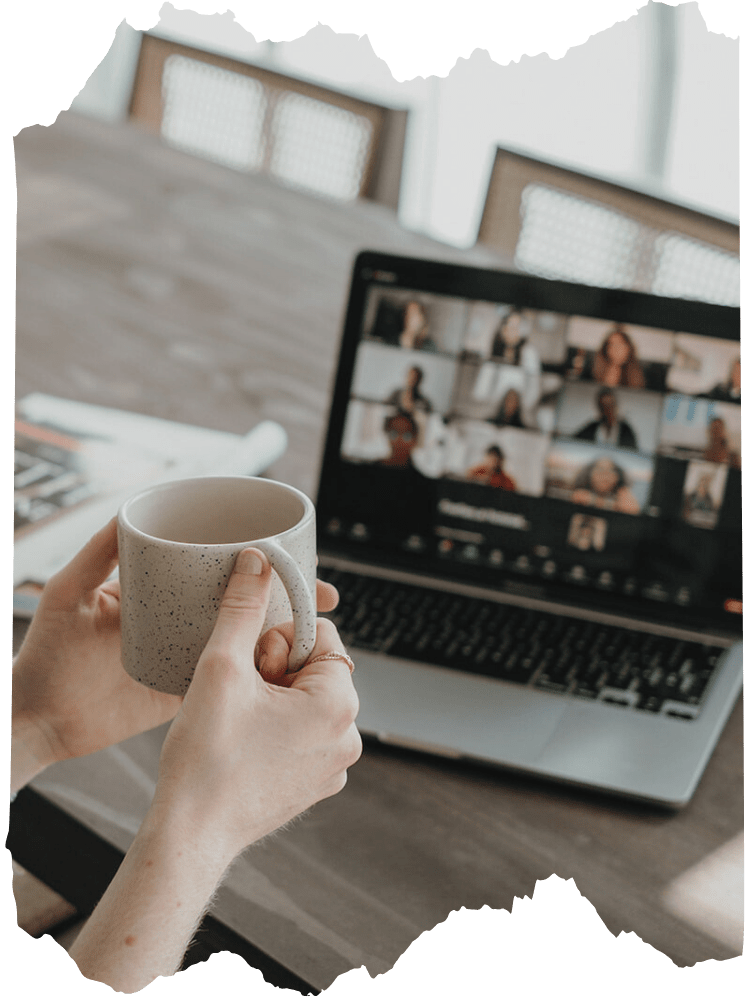 Person holding a speckled ceramic mug during a virtual meeting on a laptop at a wooden table