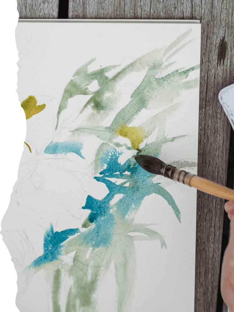 Person creating a watercolor painting of blue and green abstract botanical shapes on paper with a paintbrush.