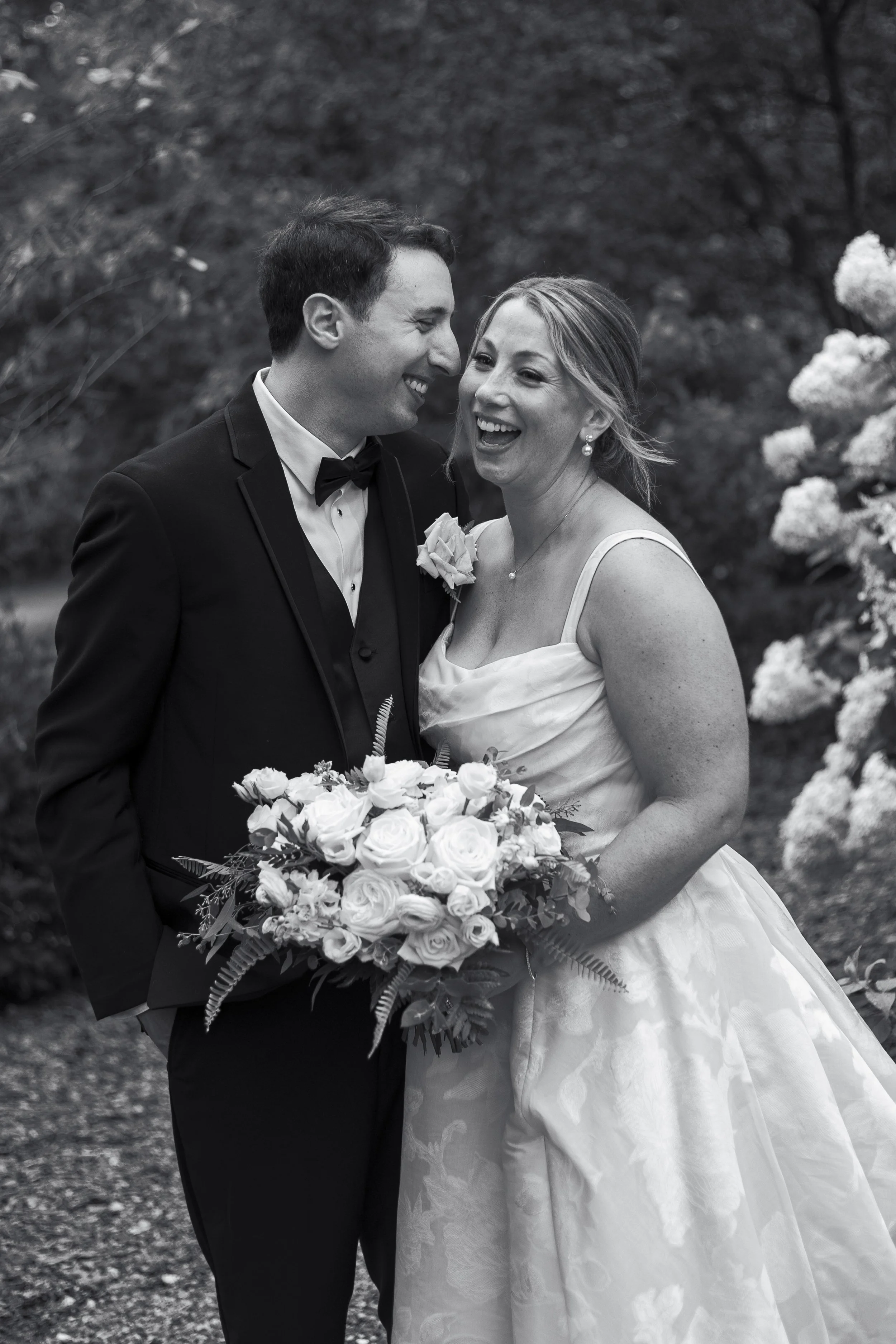 A newly married couple stands outside on a rainy day at Crossed Keys Estate in Andover, New Jersey. The bride laughs as the groom whispers a joke in her ear.  