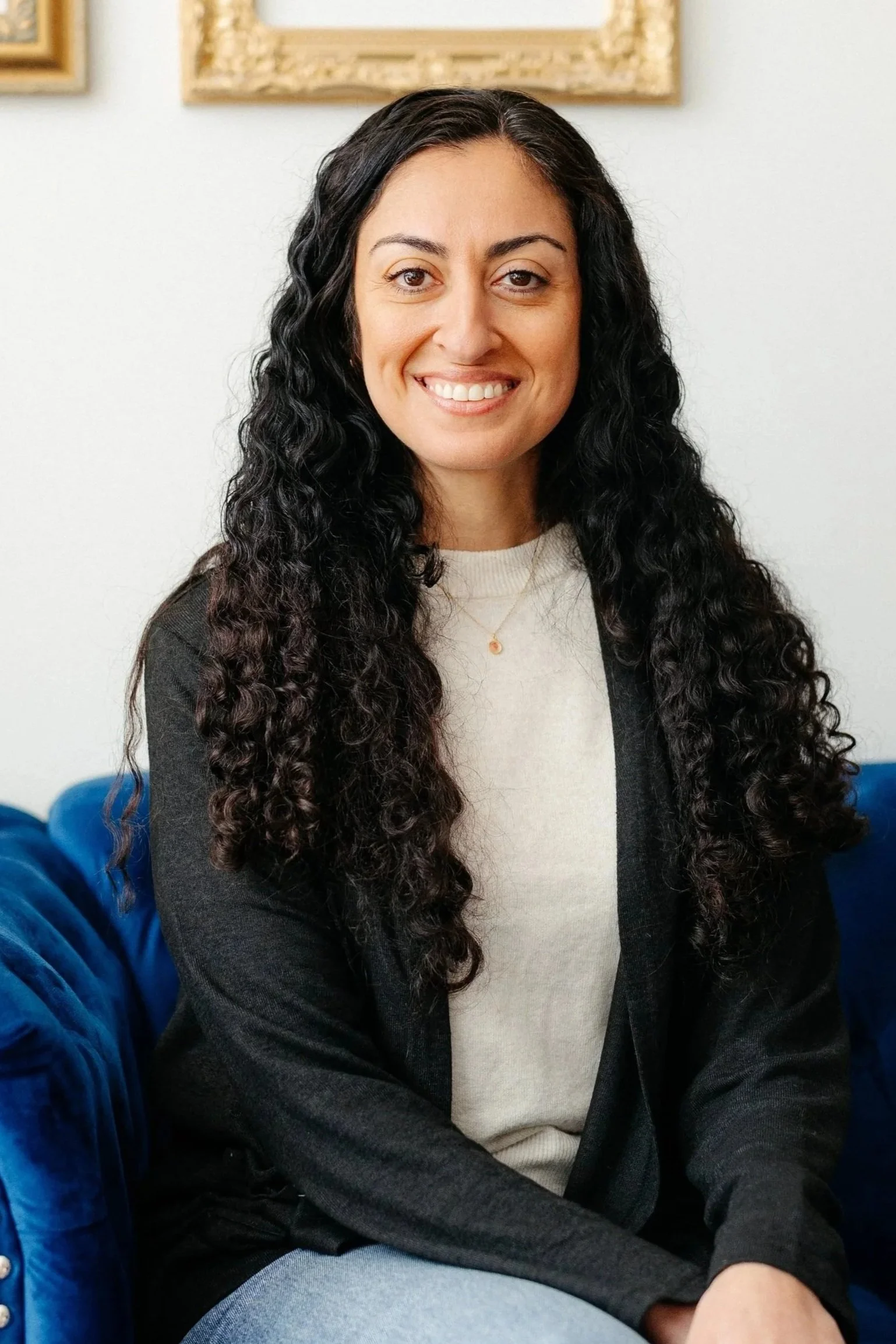 A woman with curly dark hair smiling while wearing a black cardigan with a white shirt 