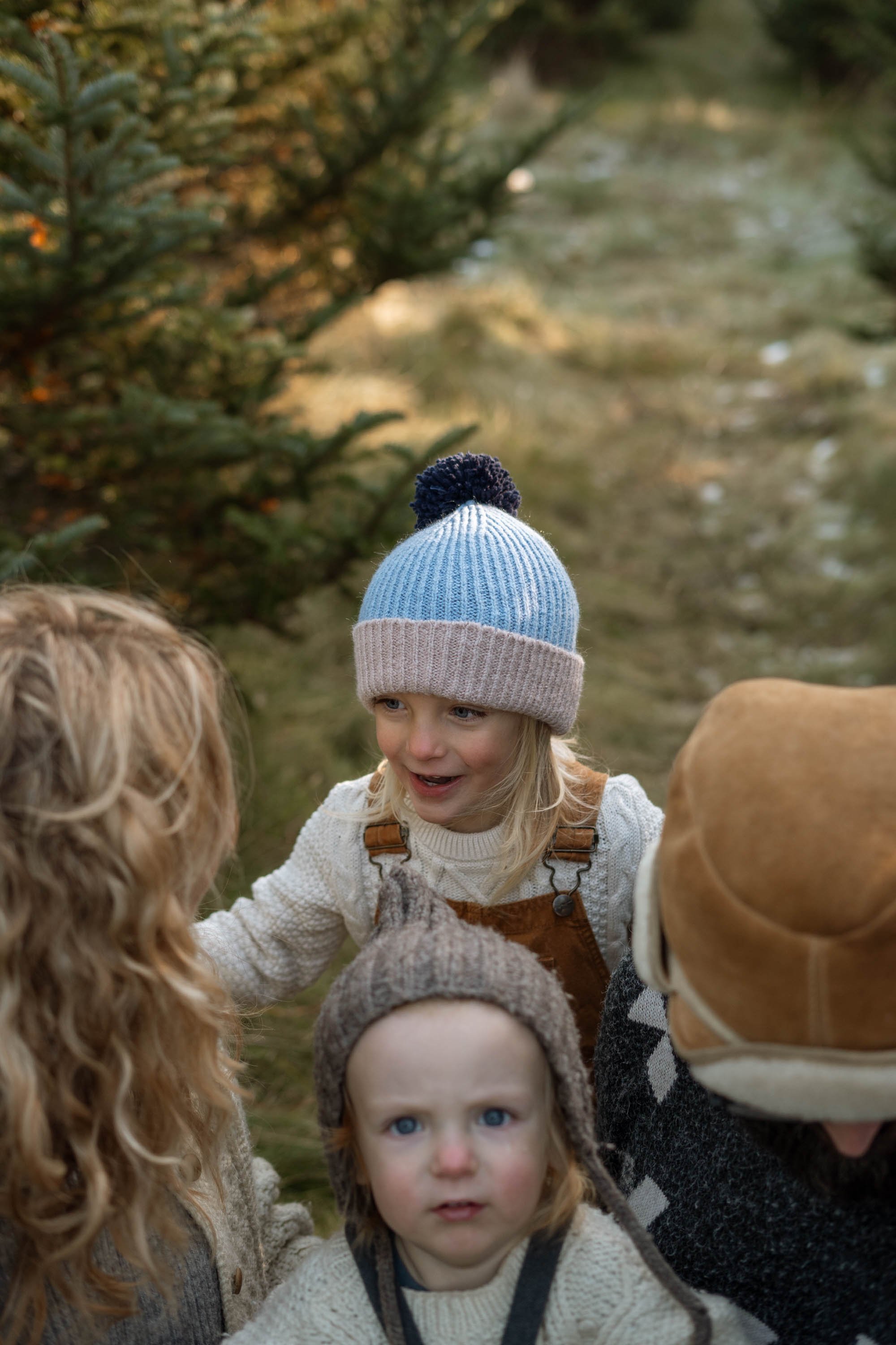 Two children and an adult in warm clothing in a forest setting, with the focus on the children wearing knit hats.