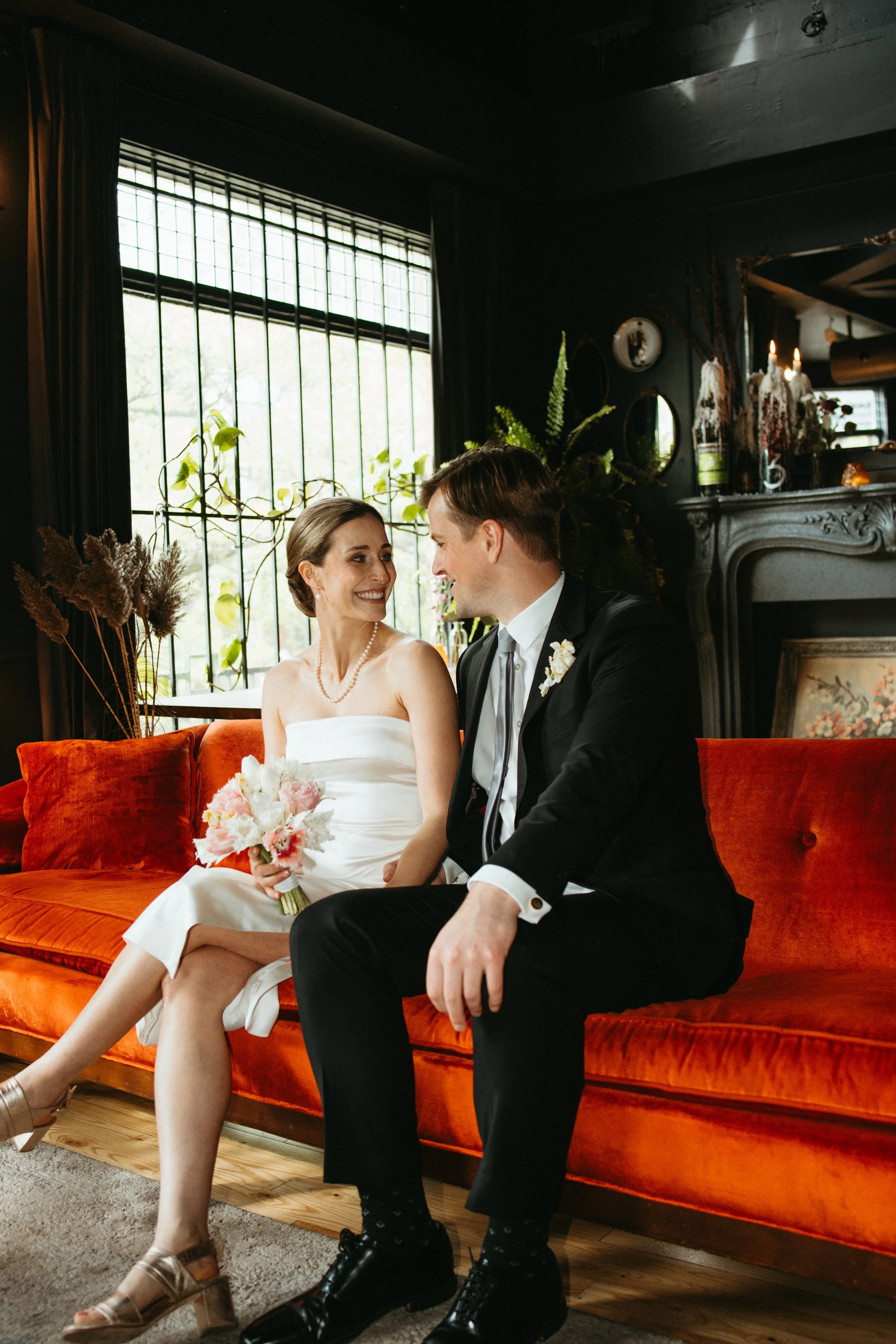 Bride in white gown with bridesmaids in floral dresses, holding bouquet, smiling indoors.