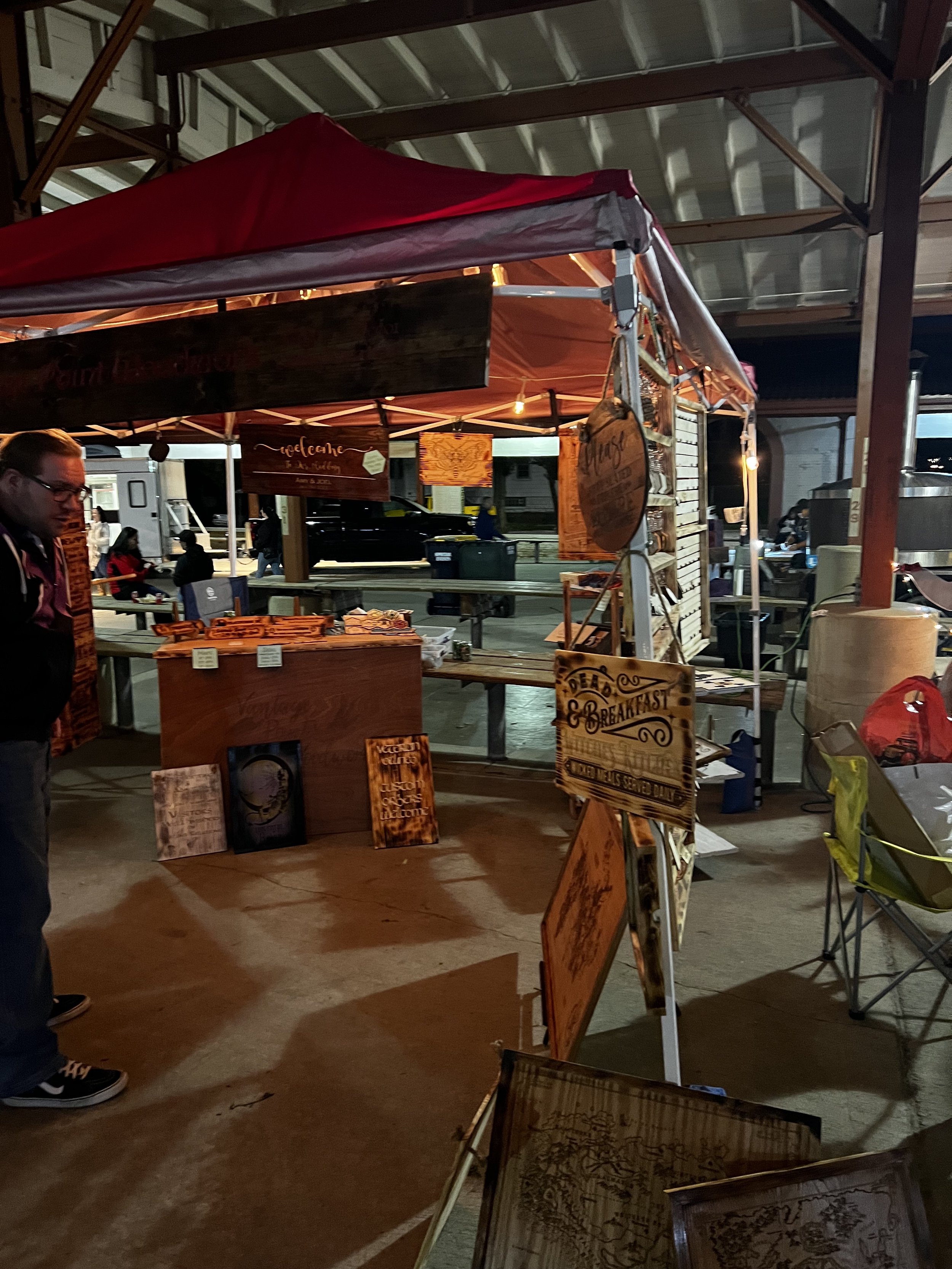 Outdoor market stall with wooden signs and decor under a red tent.