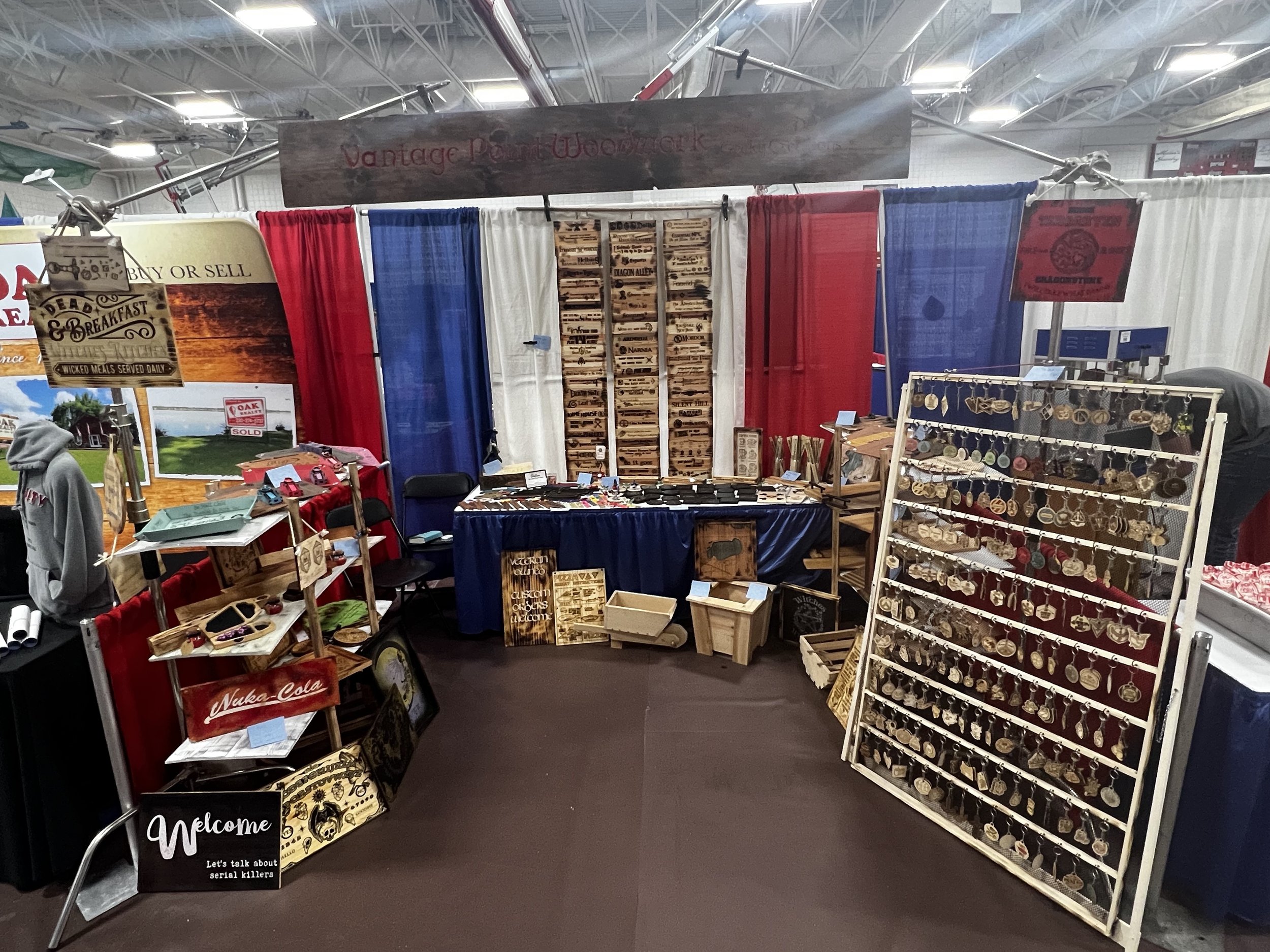 Craft fair booth showcasing handmade wooden items and jewelry with displays of engraved signs and various accessories.