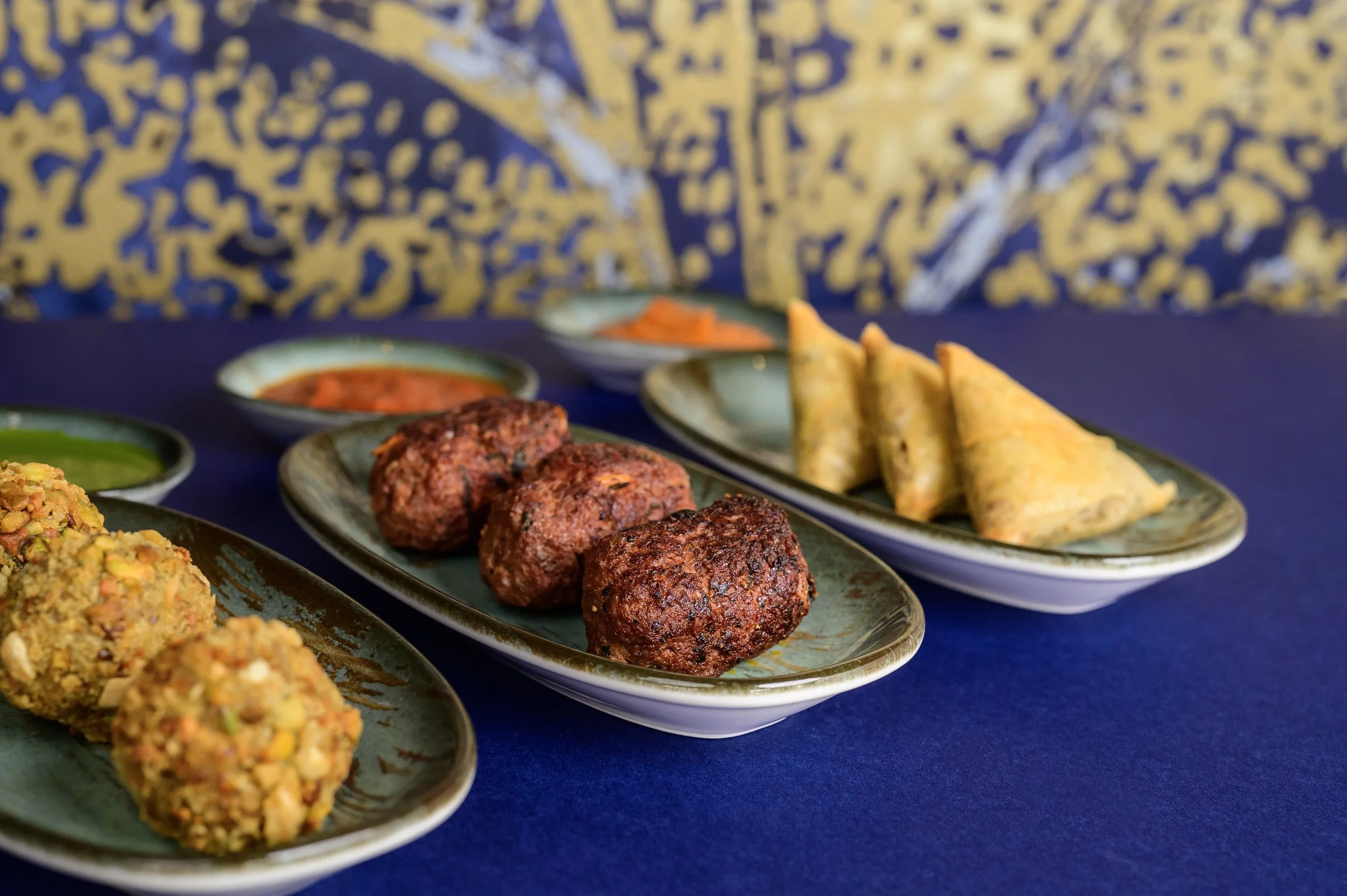 Assorted Indian appetizers including falafel, samosas, and dips on a blue table.