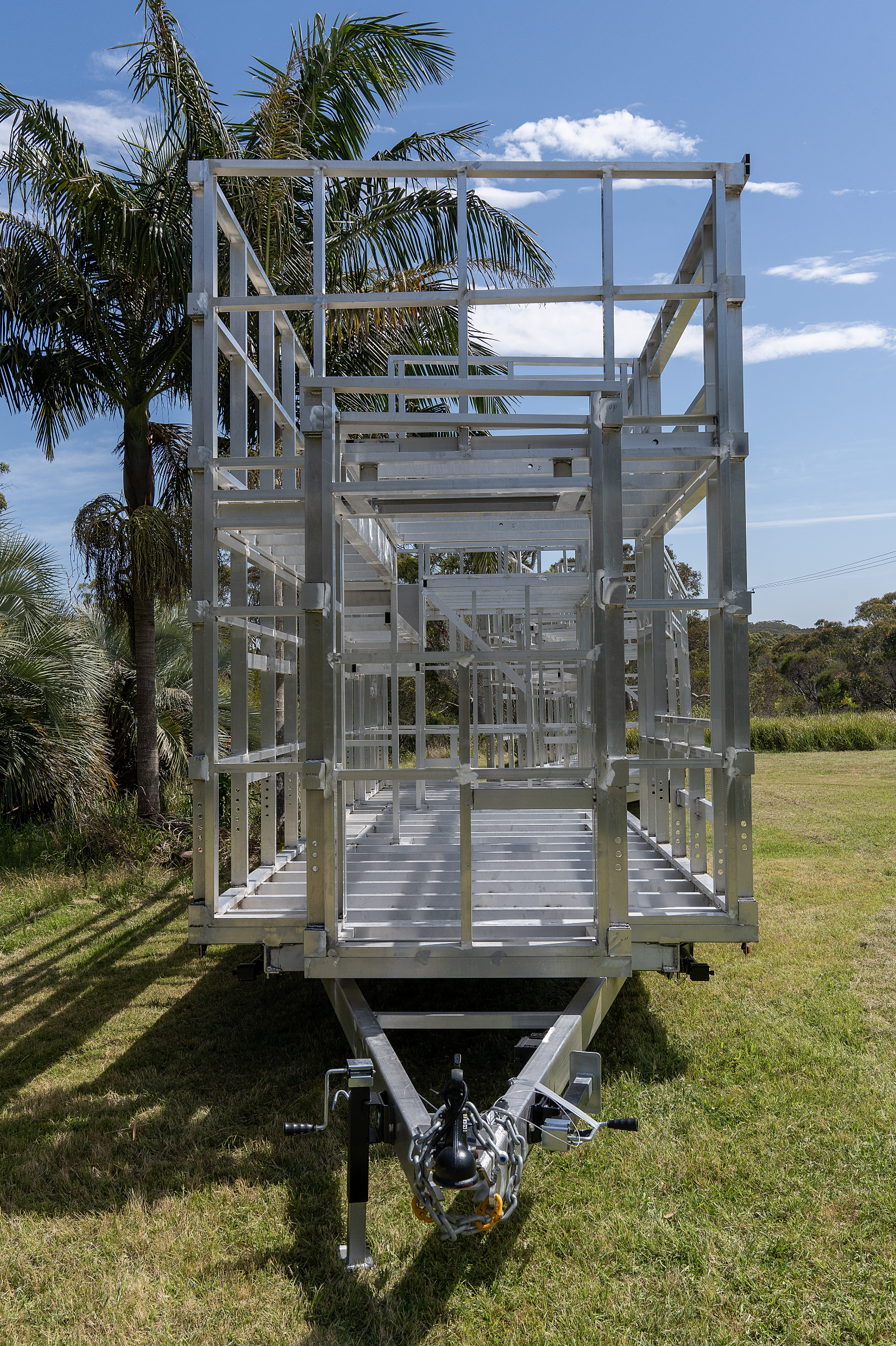 Trailer with metal frame, parked on grass with palm trees in the background.