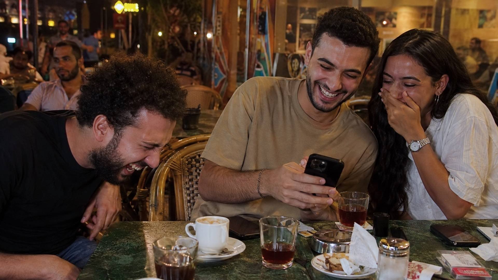 Egyptian friends laughing together at a café, showing “ana hamoot min el-de7k” as dying from laughter in everyday conversation.