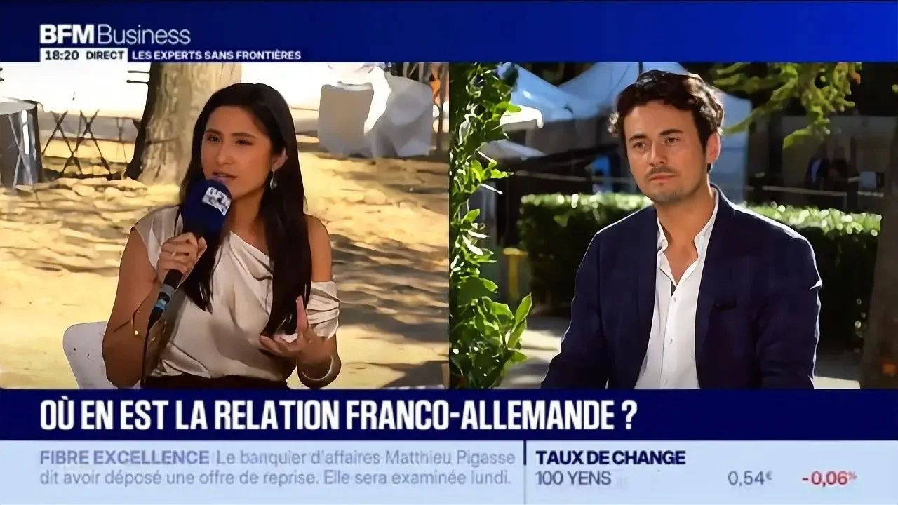 Deux personnes en interview en plein air, une femme à gauche avec un microphone, un homme à droite, dans un contexte de reportage d'affaires à la télévision.