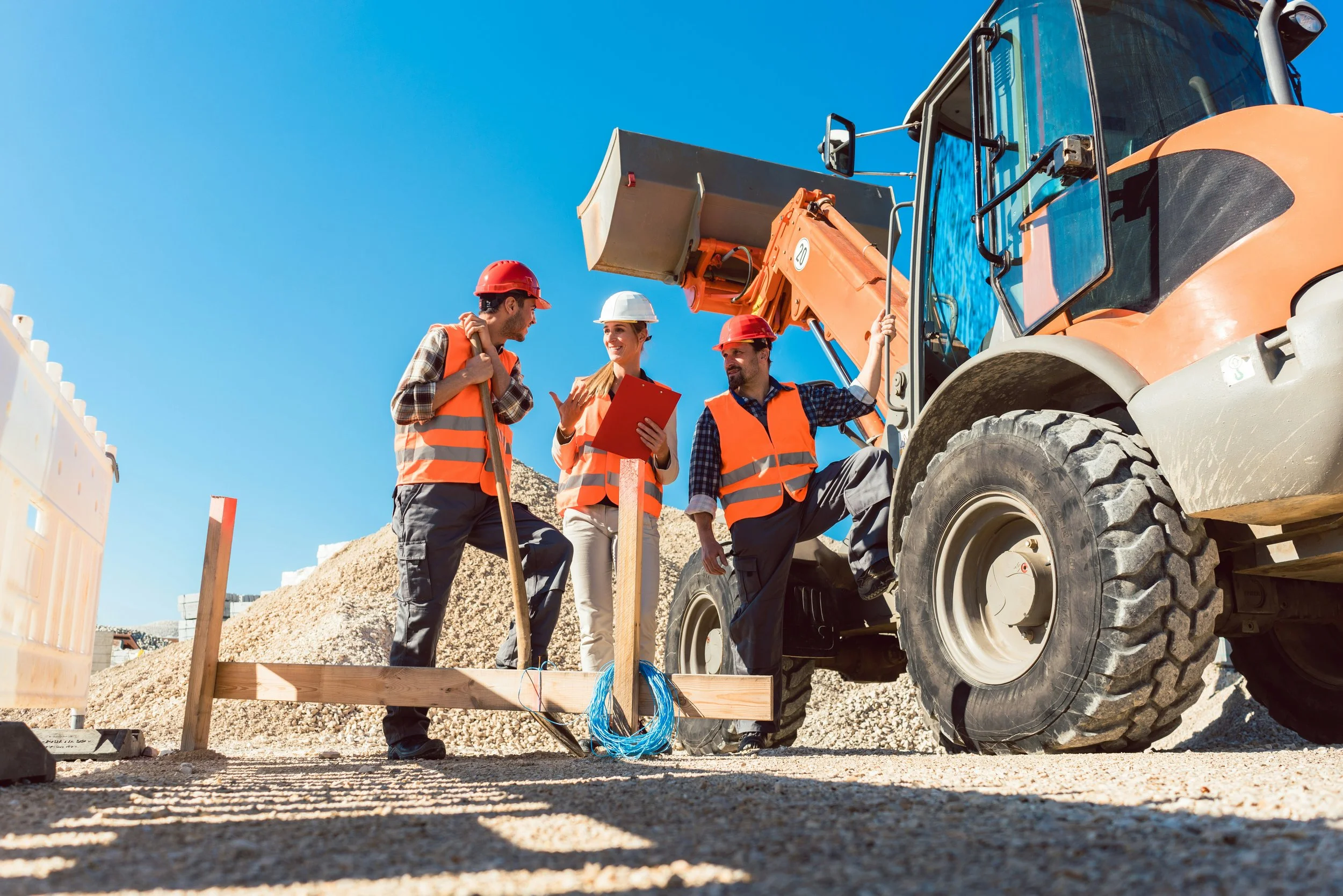 2 Männer und eine Frau in Warnwesten mit Helm auf einer Baustelle