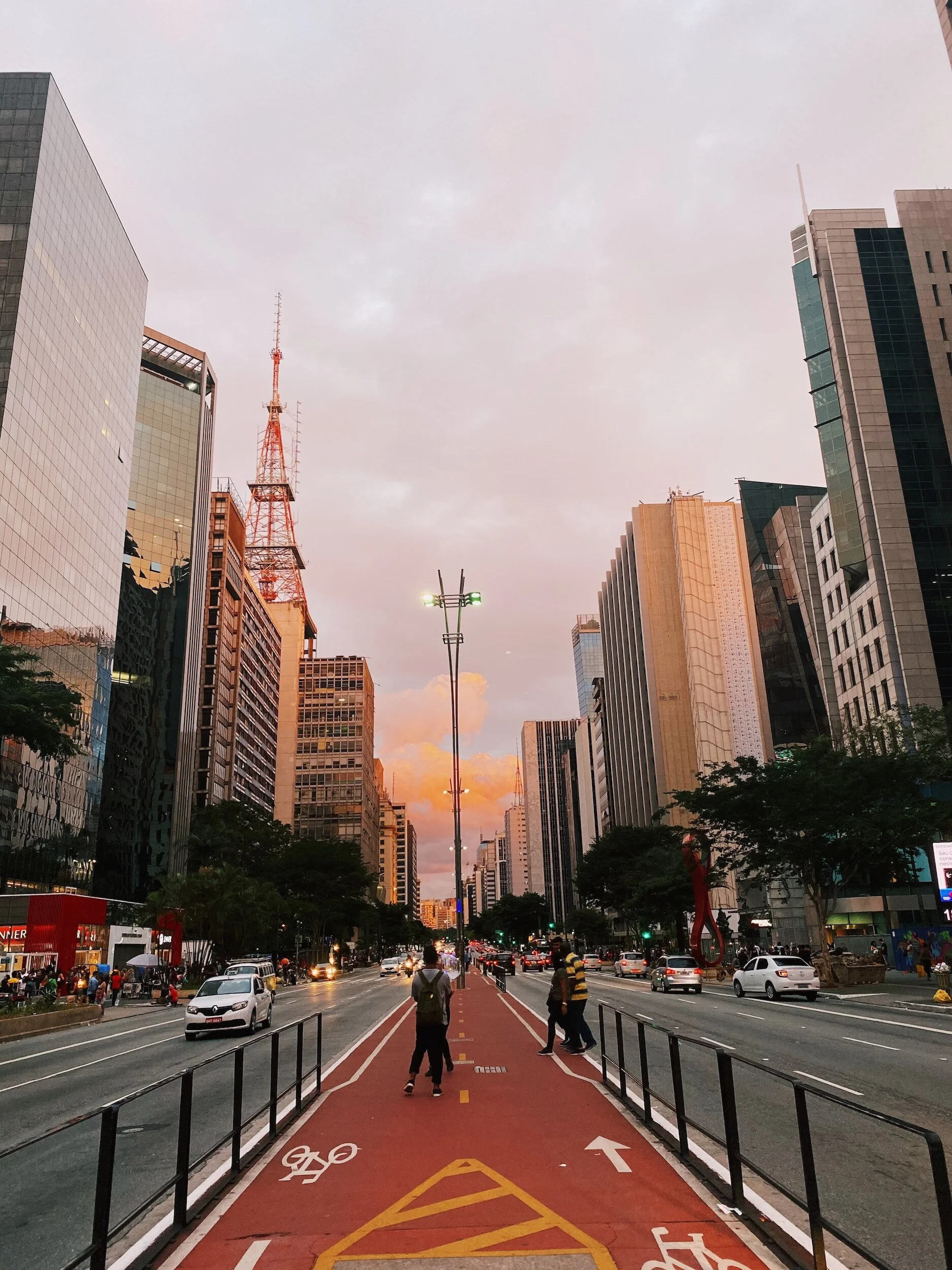 City street with a red bike lane, pedestrians, and tall buildings during sunset.