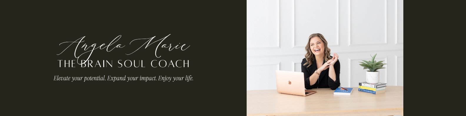 A woman sitting at a desk with a laptop, books, and a potted plant, smiling and looking away from the camera