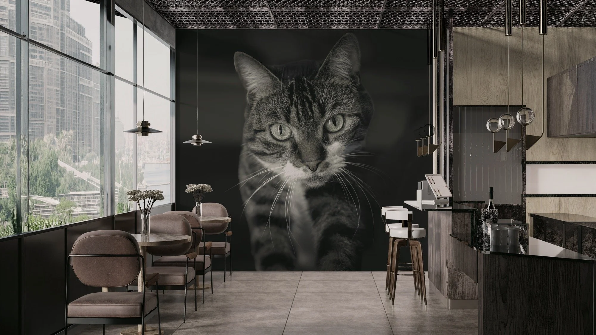 Interior of a modern cafe with a large black wall mural of a cat's face, next to windows showing a cityscape with tall buildings, a table with pink chairs, pendant lights, and a bar counter.