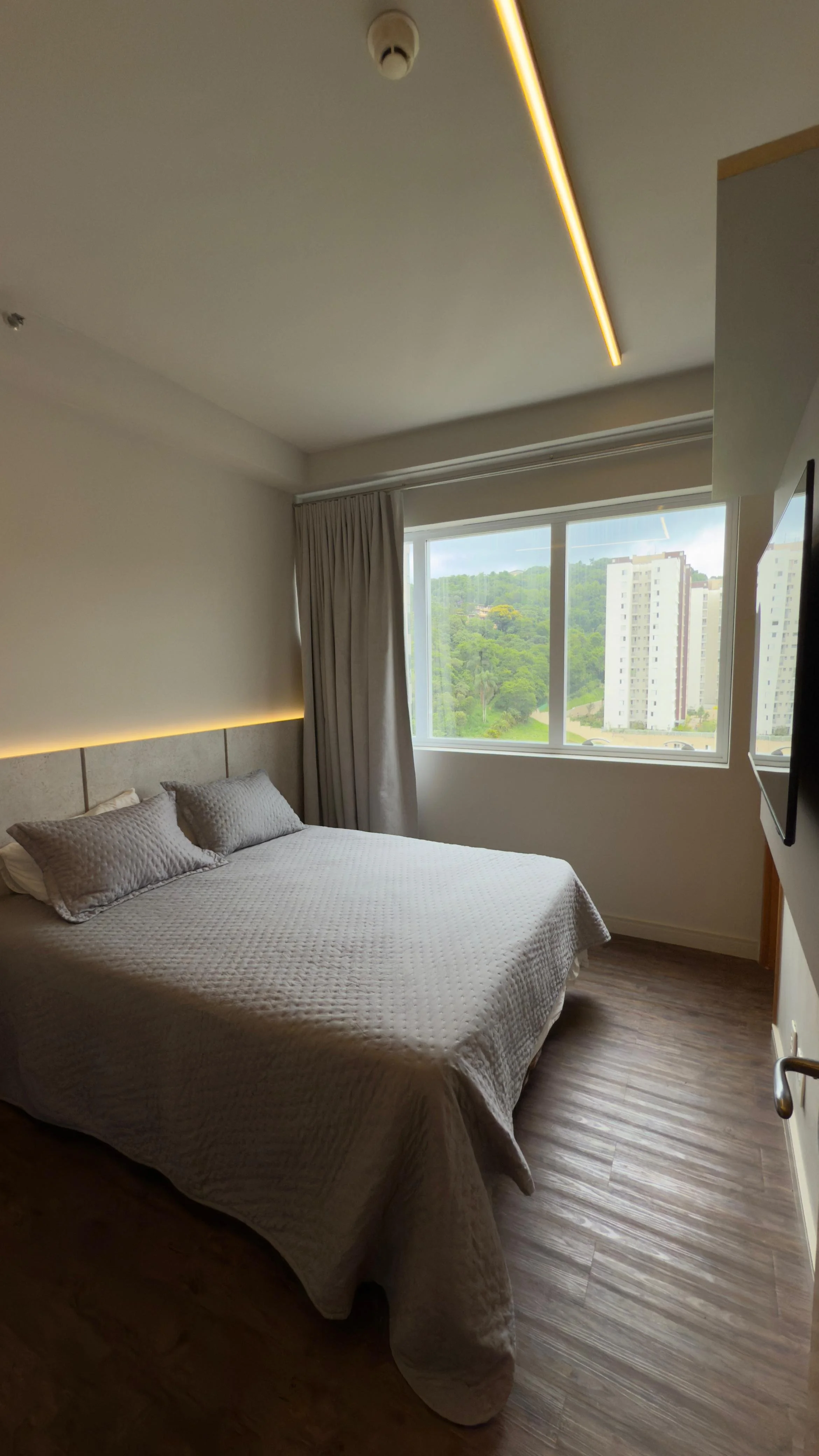 Sala de espera em um ambiente de hotel ou escritório, com poltronas de couro marrom, sofá branco com almofadas e cadeiras de madeira, plantas decorativas e iluminação indireta.
