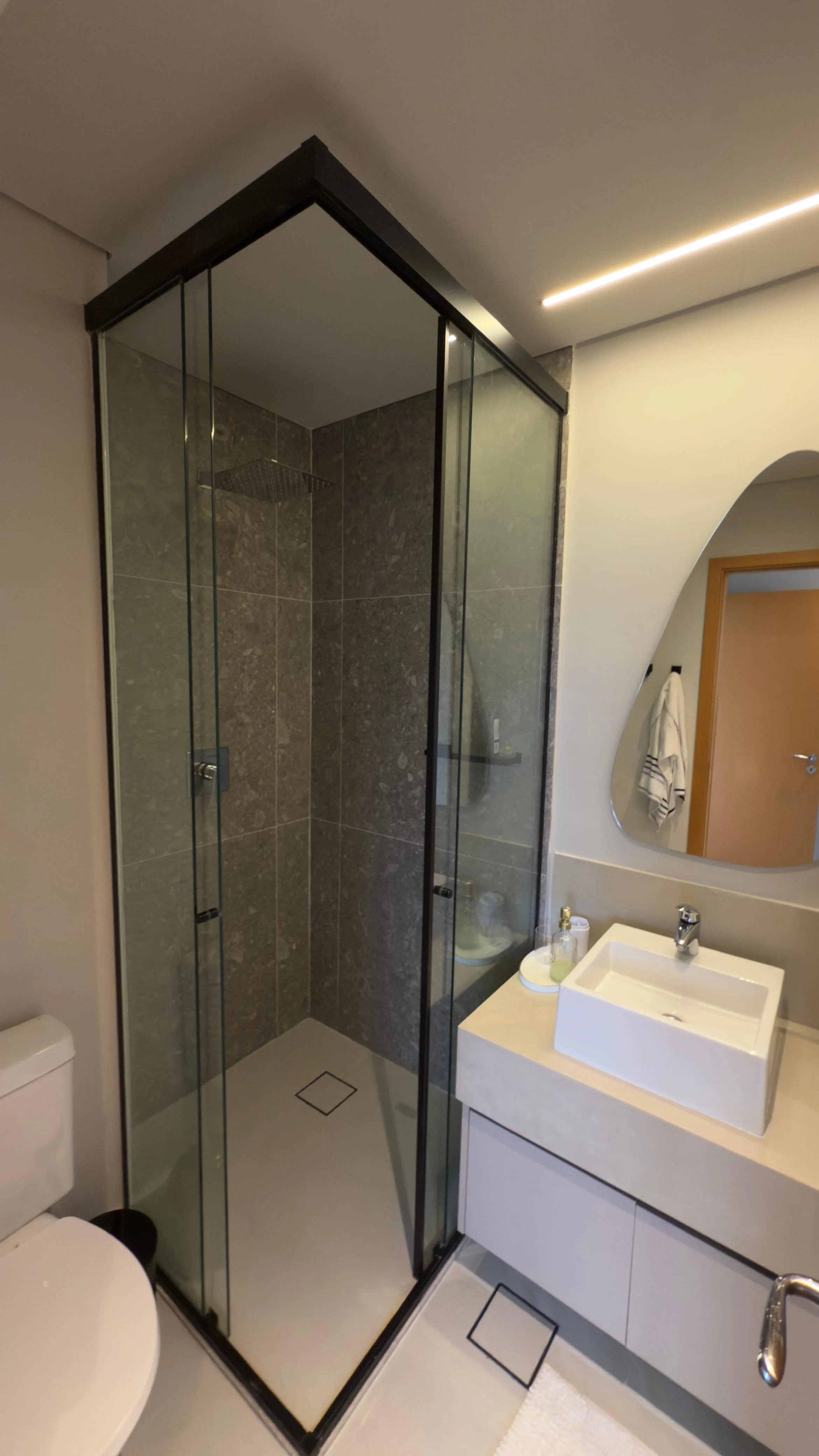 Imagem de uma cozinha moderna com paredes brancas, bancada preta e armários brancos. Há uma área de pia com backsplash de azulejos pequenos em tons de preto e branco. Um fogão de cooktop está na bancada preta, ao lado de uma parede que leva a um quarto visível ao fundo.