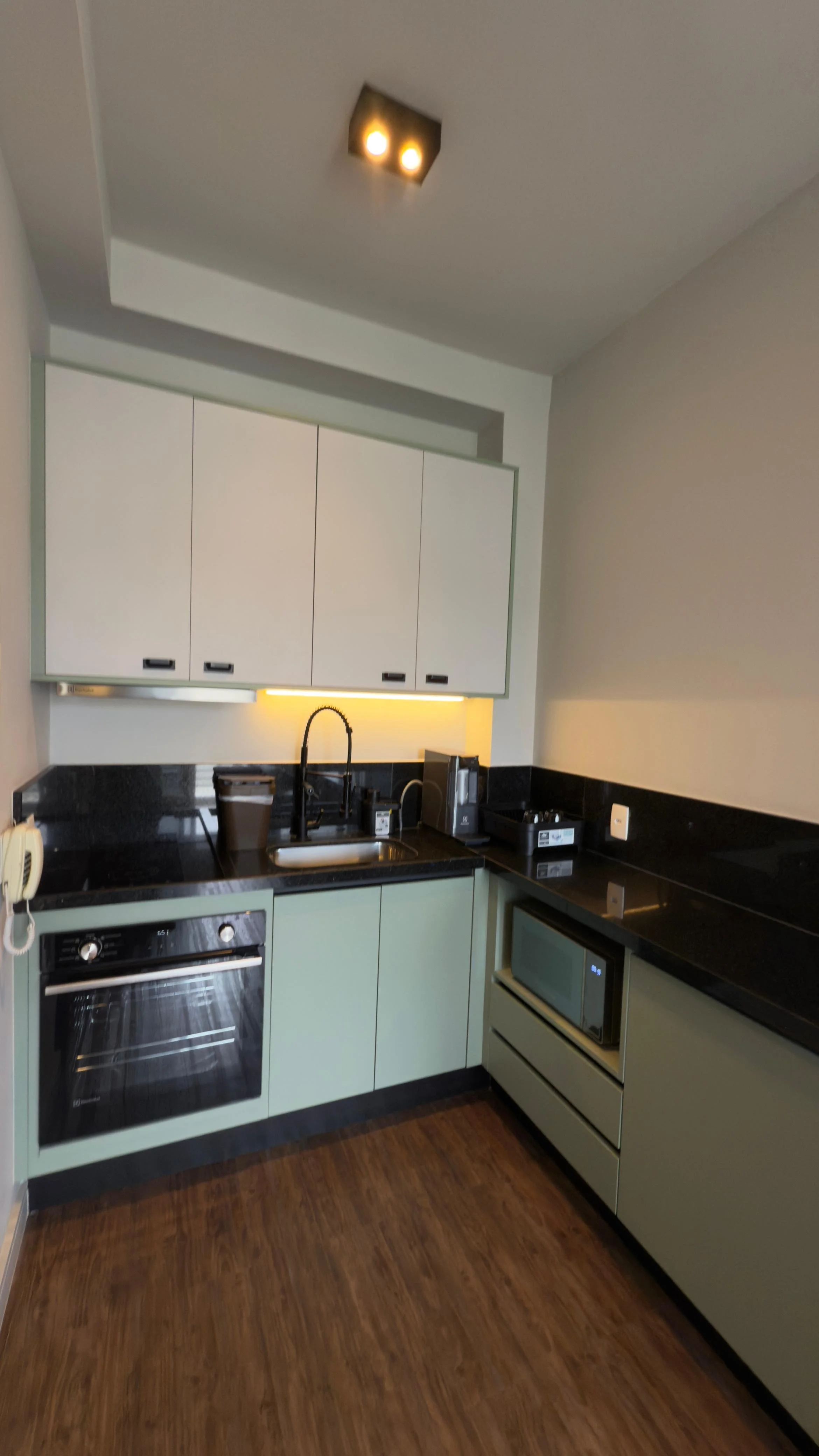 Área de lavanderia com várias máquinas de lavar roupa brancas alinhadas, pia com torneira, prateleiras azuis com livros e uma parede de fundo vermelha com quadros e uma TV.