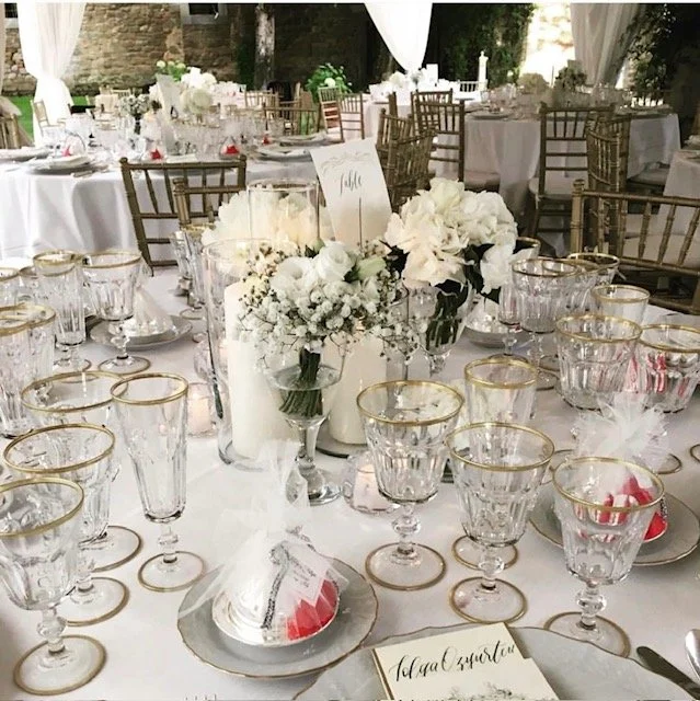 Dekket festbord med hvite blomsterarrangementer, glass, tallerkener og pynt, klare for en høytidsfeiring eller bryllup.