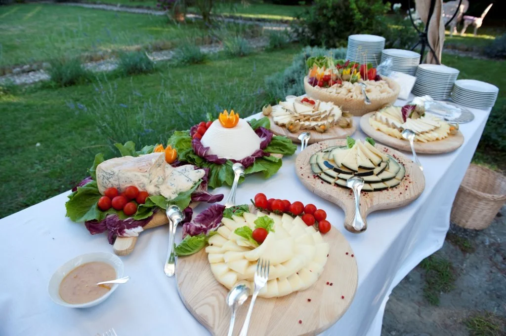 Uendelig buffet med ulike oster, frukt og salater på et dekket bord utendørs.