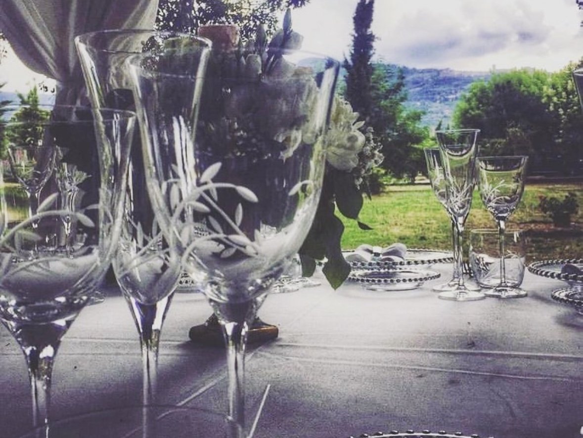  glass med blomster på en dekket bord med et landskap i bakgrunnen