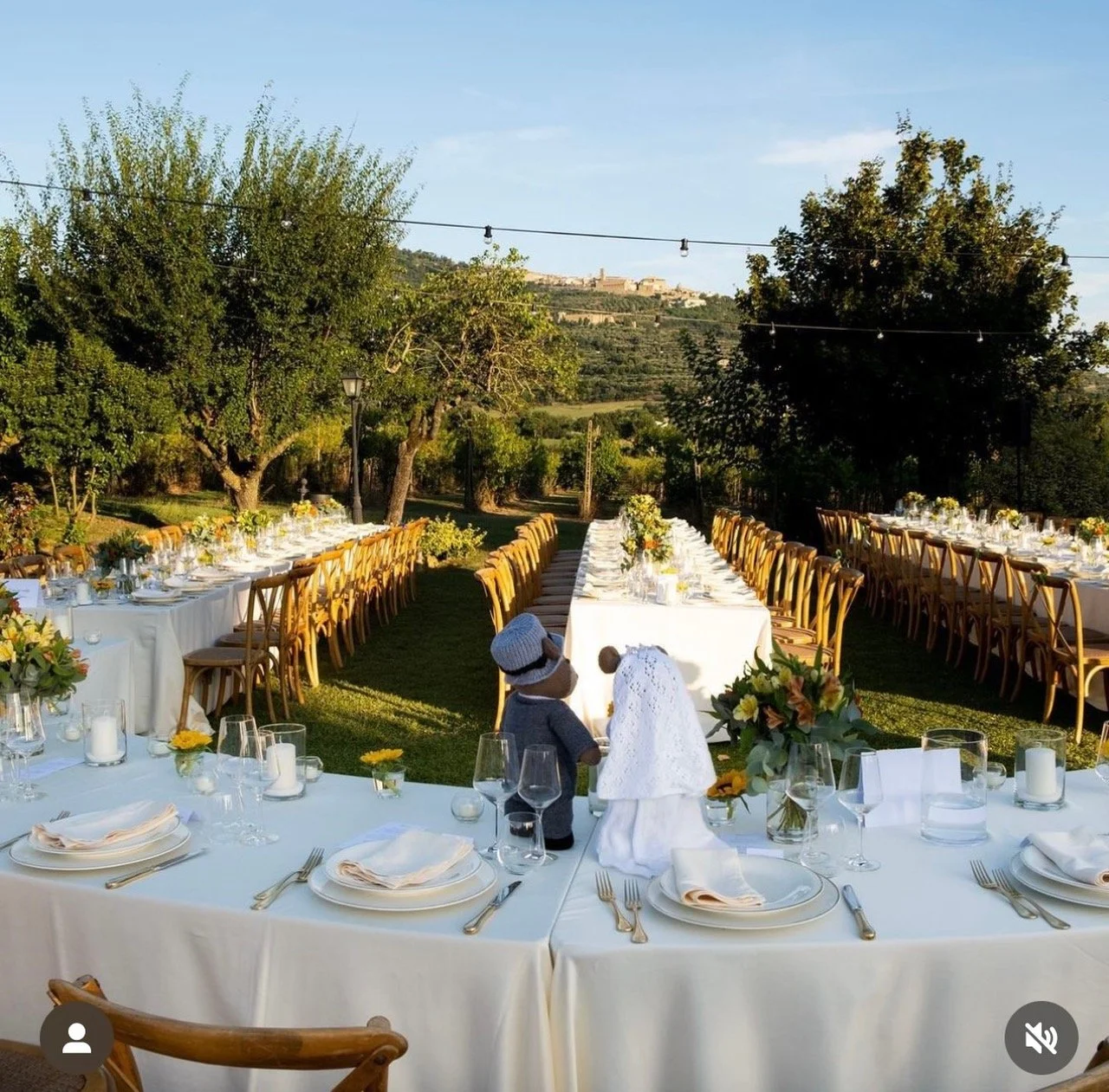 Outdoor wedding reception with long, decorated tables and chairs arranged on grass, under a clear blue sky.