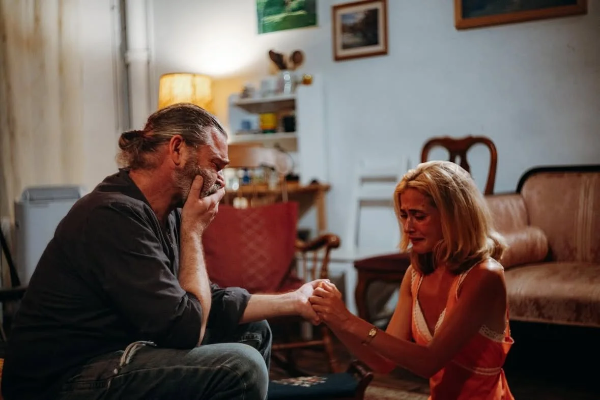 A man and woman sitting on the floor in a living room holding hands, showing emotional distress.